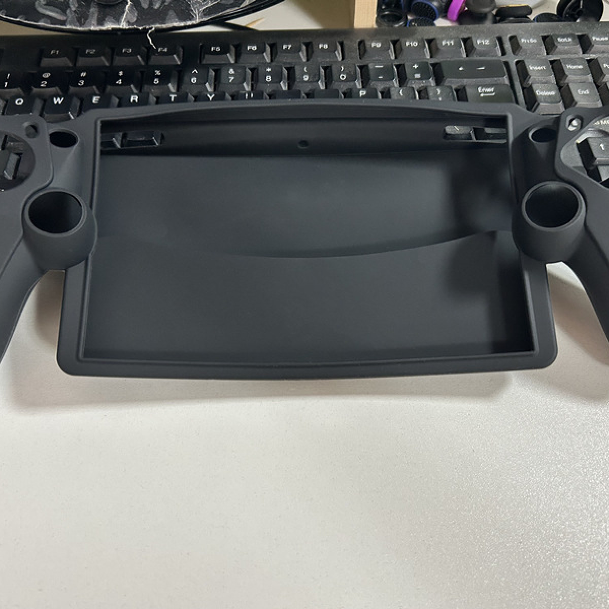 Un telaio nero per console di gioco su una superficie bianca. Una tastiera sullo sfondo.