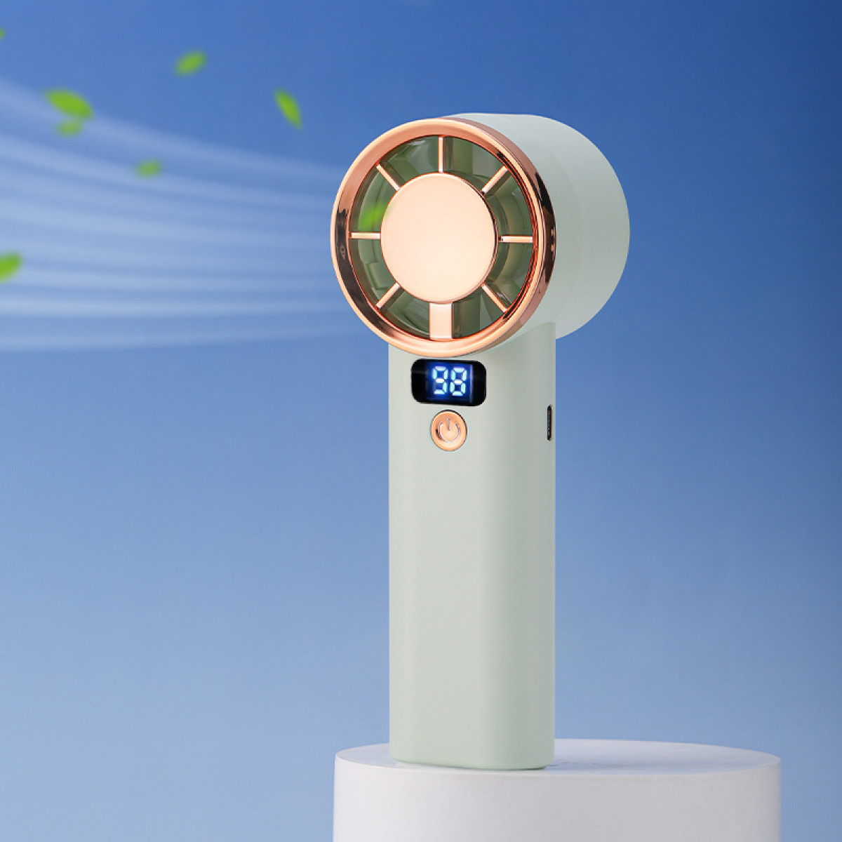 Przenośny wentylator ze złotym pierścieniem, białą obudową i niebieskim wyświetlaczem cyfrowym, na niebieskim tle gradientowym, z zielonymi liśćmi.