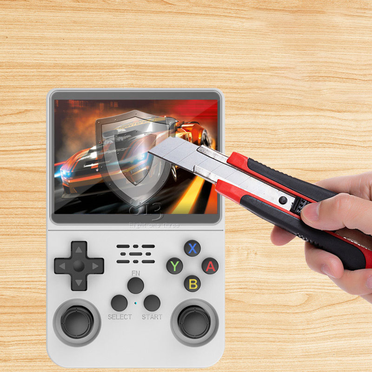 Przenośna konsola do gier z ekranem wyświetlającym grę wyścigową. Ręka trzyma nożyk do tapet nad ekranem.