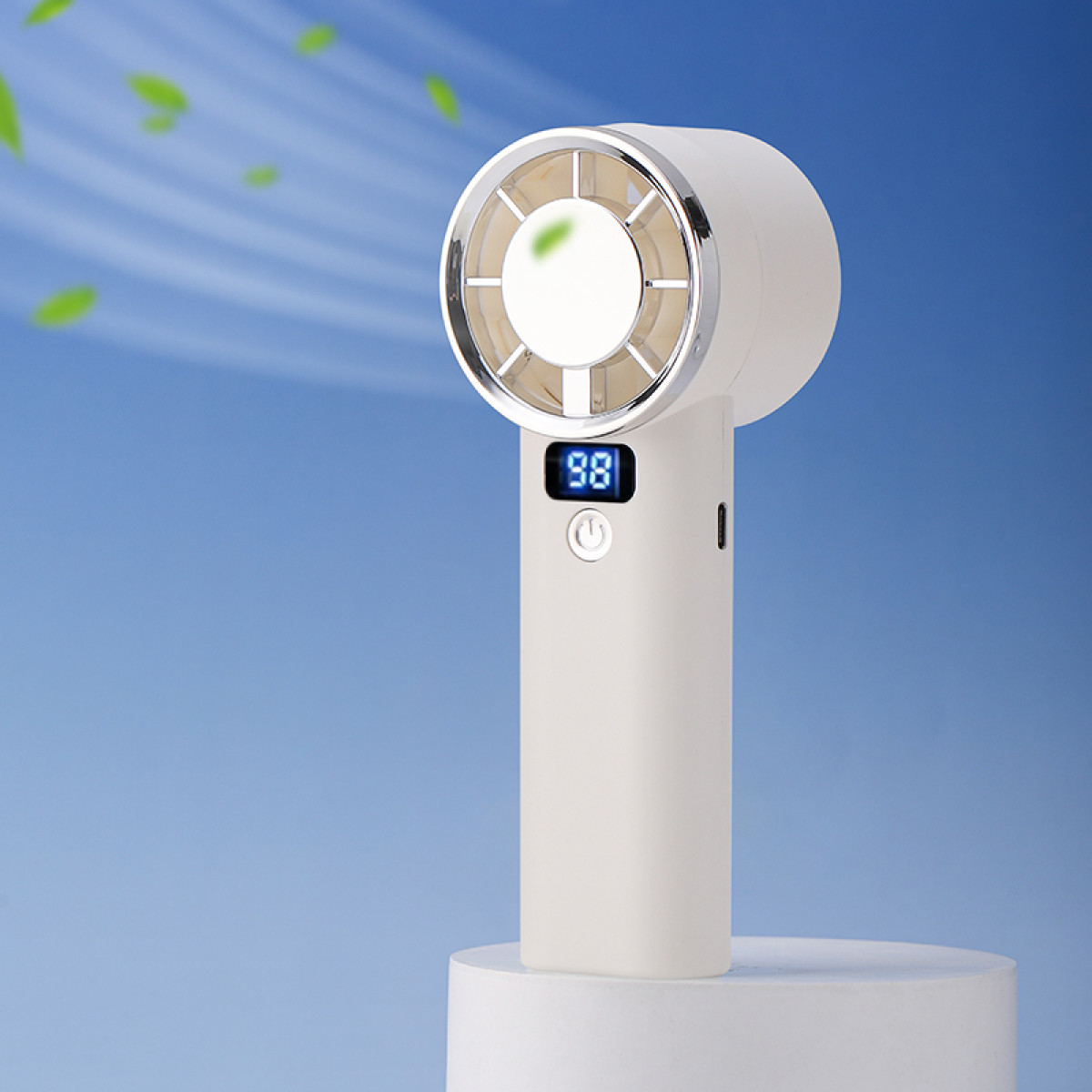 Biały wentylator ręczny z cyfrowym wyświetlaczem '98'. Stoi na białym cokole, z niebieskim tłem i zielonymi elementami liści.