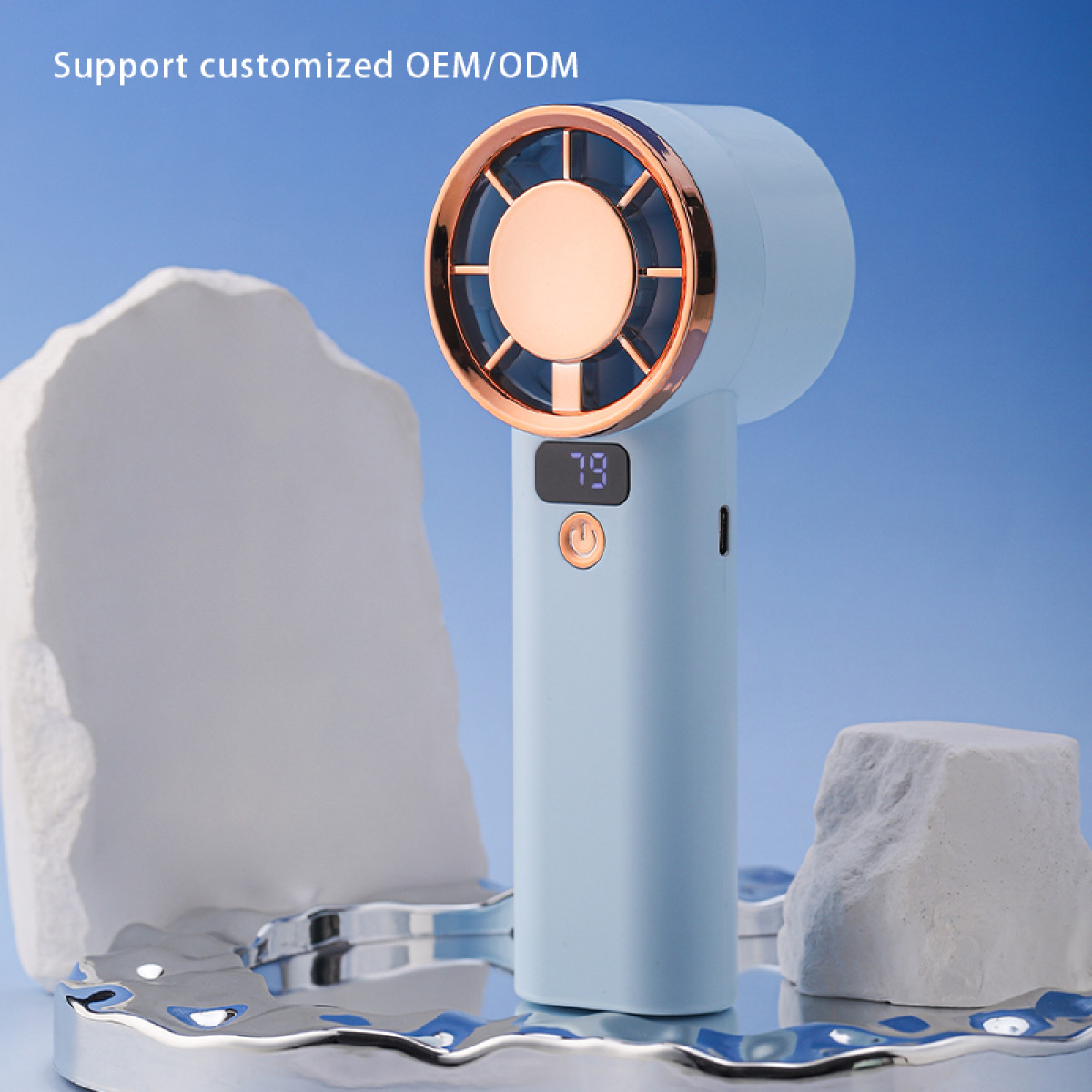 Jasnoniebieski przenośny wentylator ze złotymi i miedzianymi akcentami. Posiada cyfrowy wyświetlacz z napisem '79' i stoi na odblaskowej powierzchni.