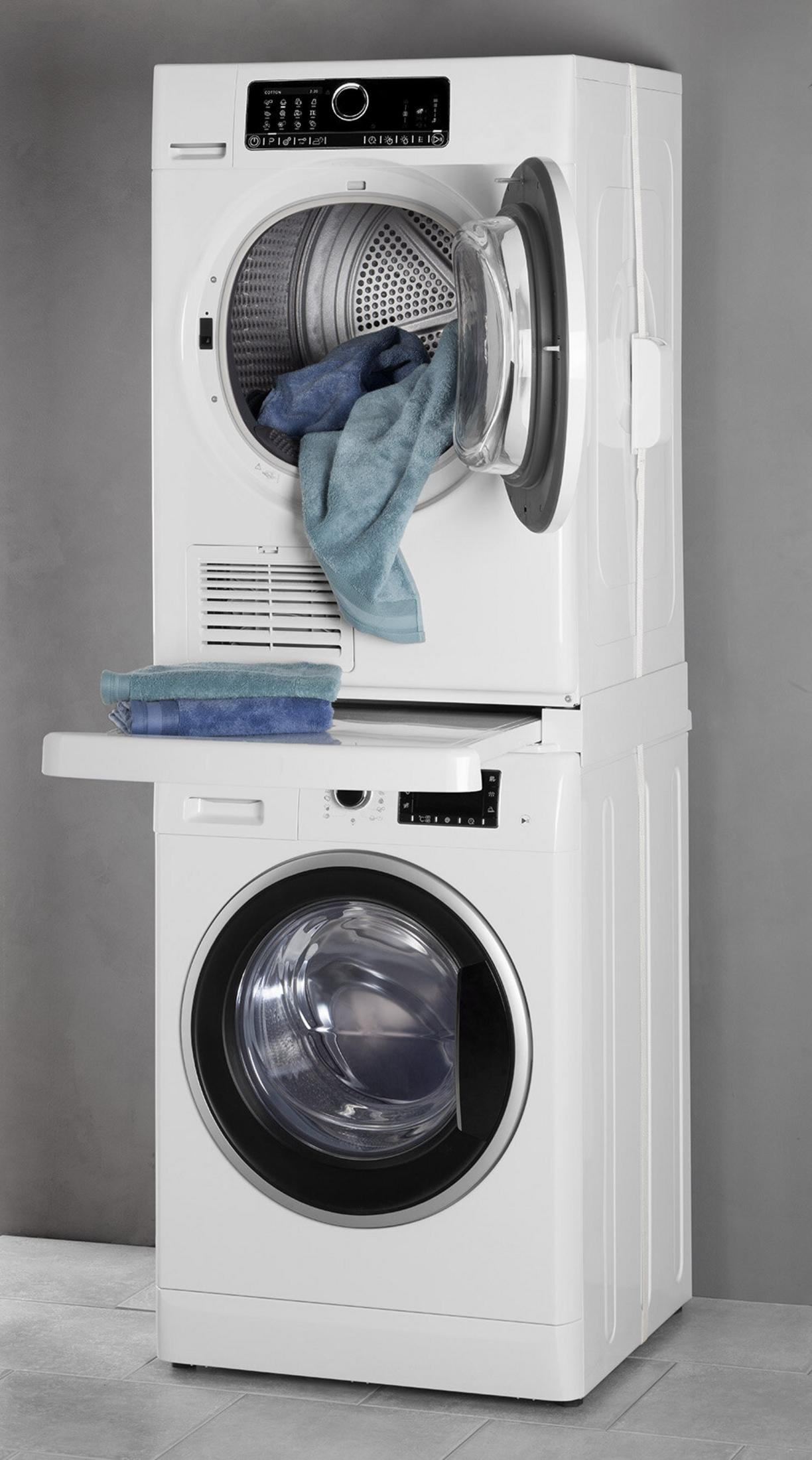 Een witte gestapelde wasmachine en droger. De drogerdeur staat open met handdoeken erin. Meer handdoeken liggen op de plank.