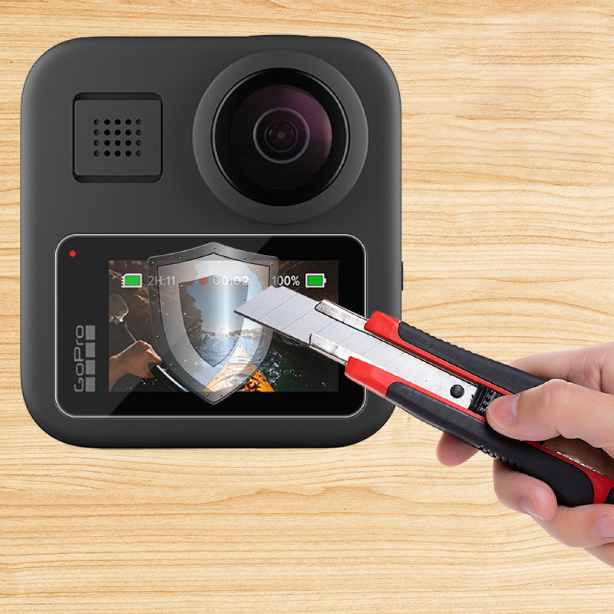 Una mano sostiene un cúter, cortando un protector de pantalla en una cámara GoPro. La cámara es negra, sobre una superficie de madera.