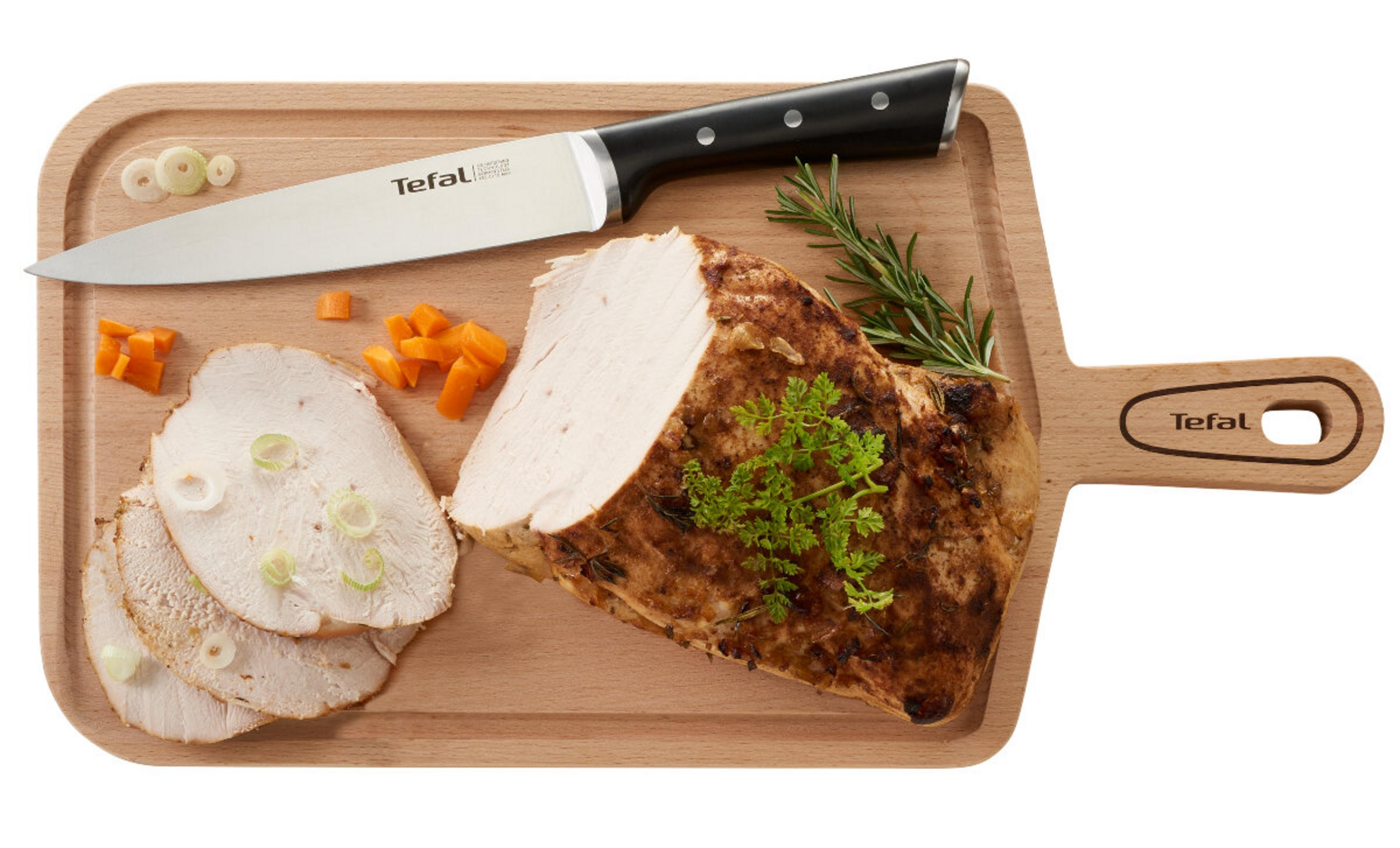 Una tabla de cortar con pavo asado, un cuchillo, rodajas de pavo, zanahorias picadas y aros de cebolla.