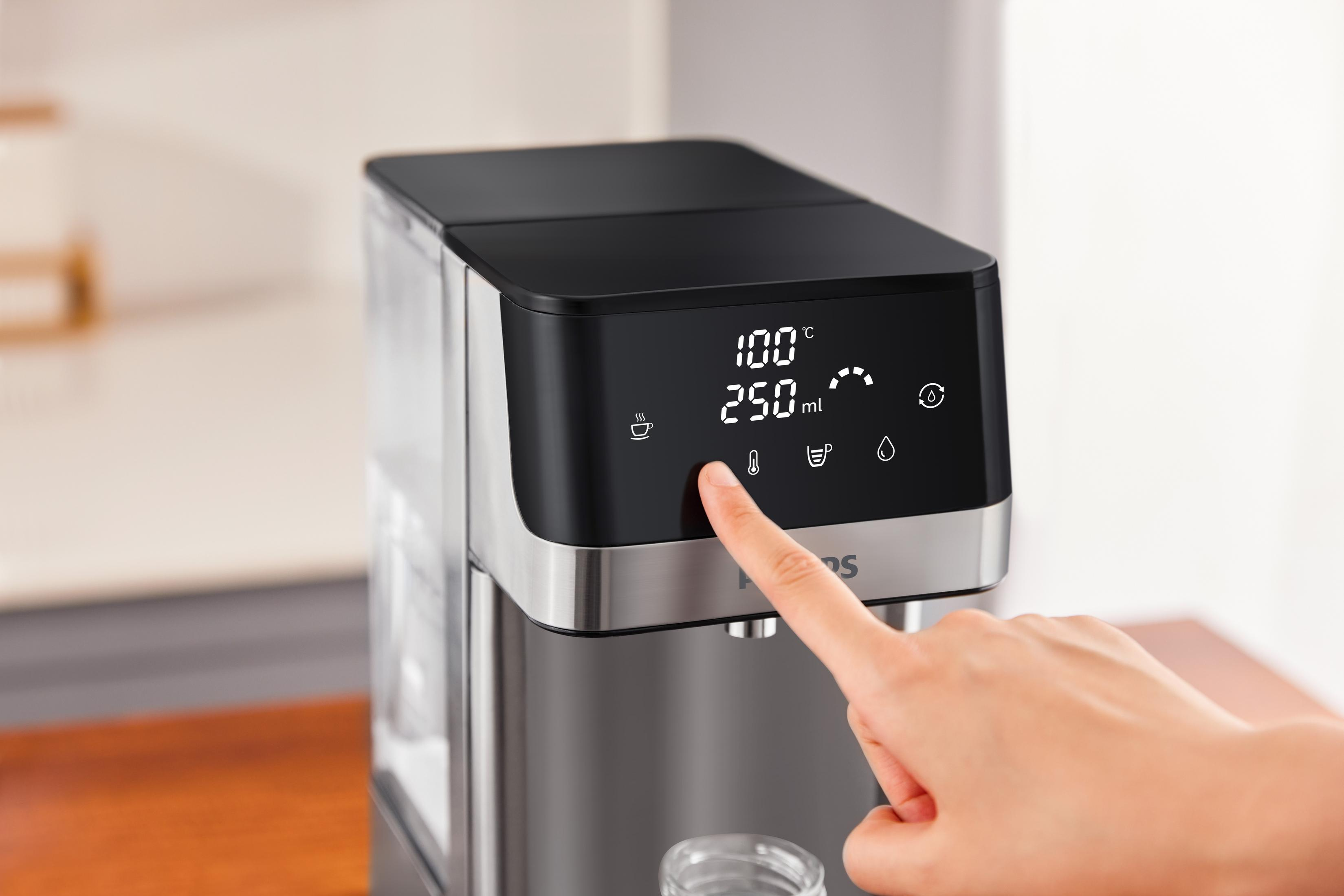 Eine Hand drückt eine Taste auf einem schwarzen und silbernen Wasserspender. Das Display zeigt Temperatur, Volumen und Symbole.