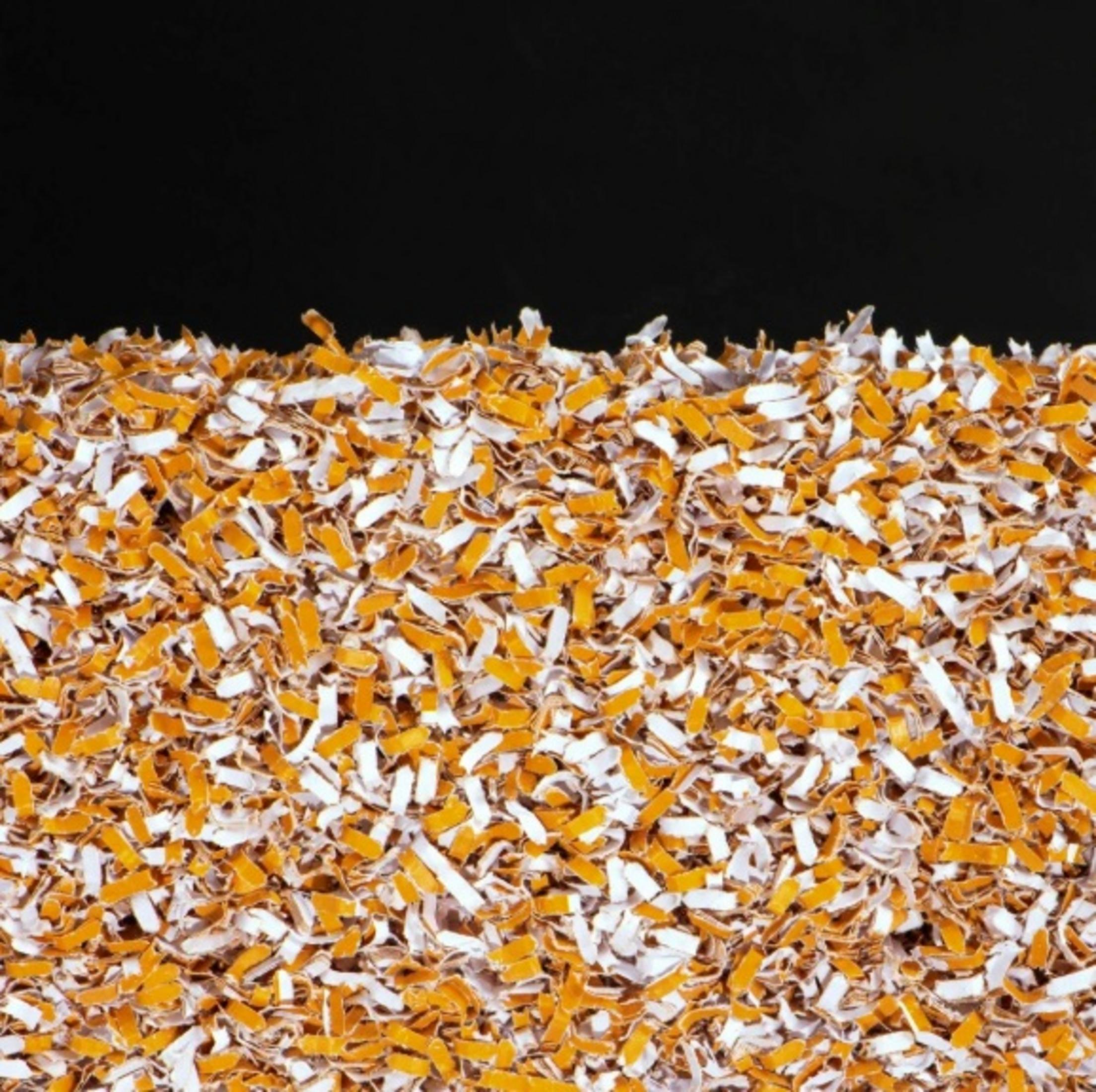L'immagine mostra un primo piano di materiale triturato arancione e bianco, con sfondo nero.