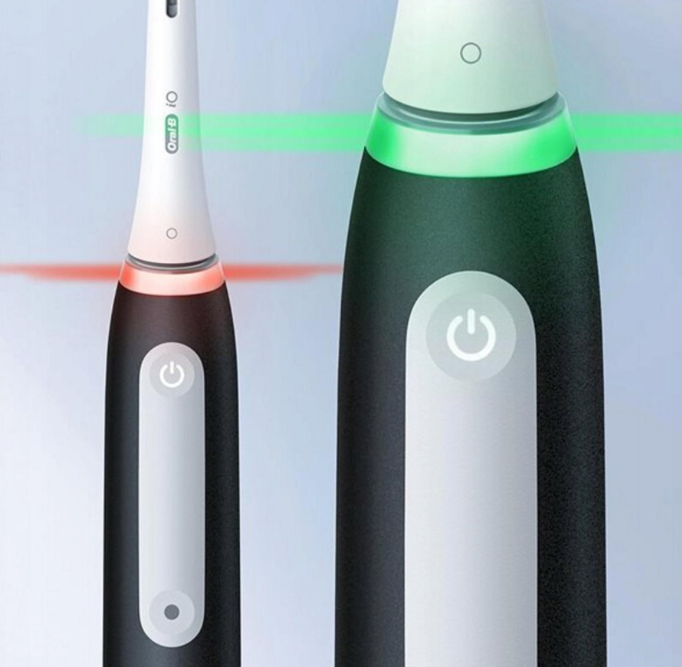 Two electric toothbrushes with different colors and glowing lights. Power buttons are visible on the handles.