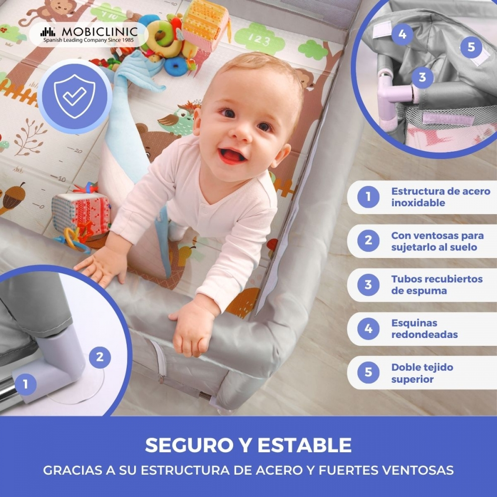 Un bebé sonríe en una cuna. Juguetes rodean al bebé. La cuna tiene lados acolchados y es segura y estable.