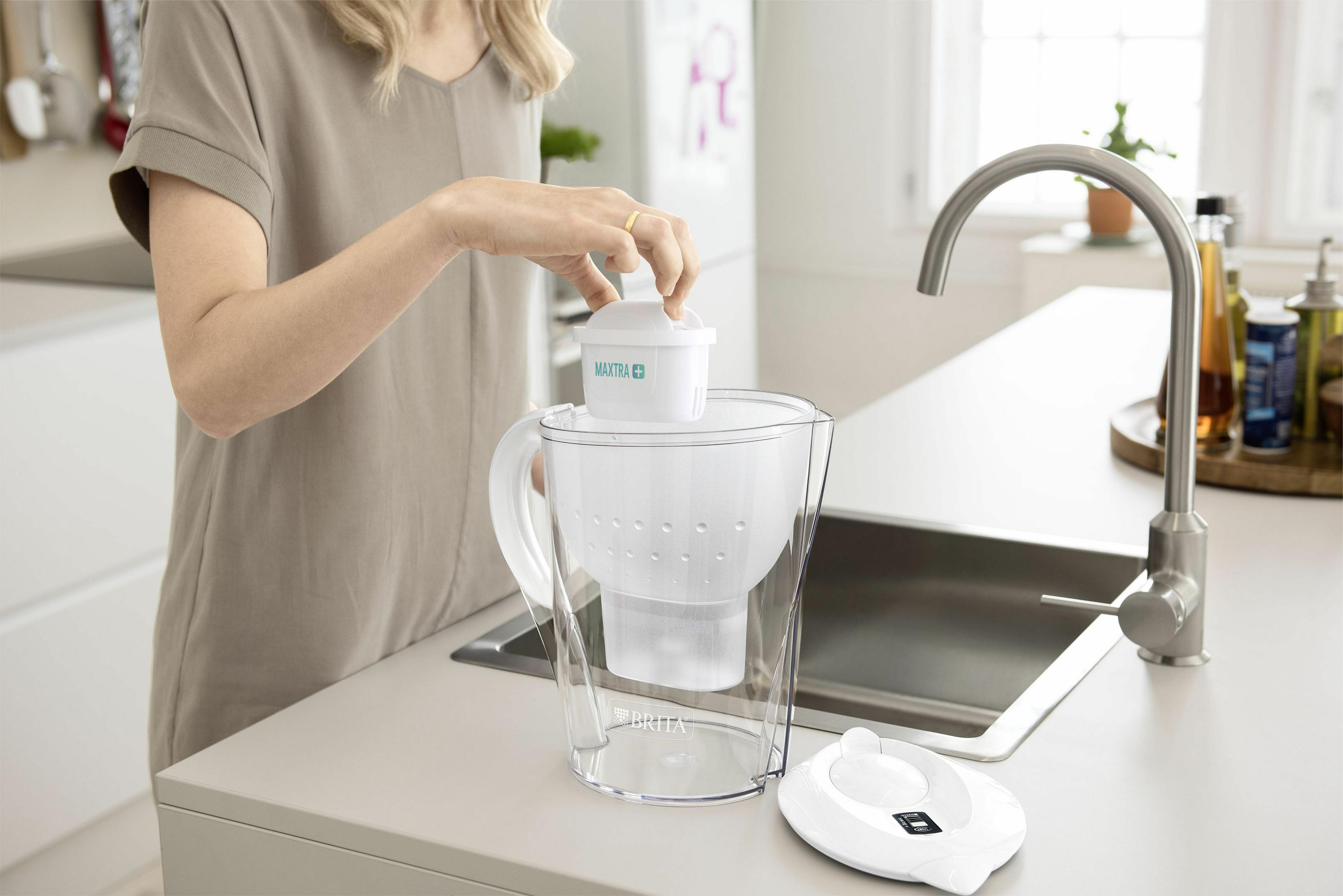 Eine Person setzt einen Wasserfilter in einen Wasserkrug in einer Küche ein.