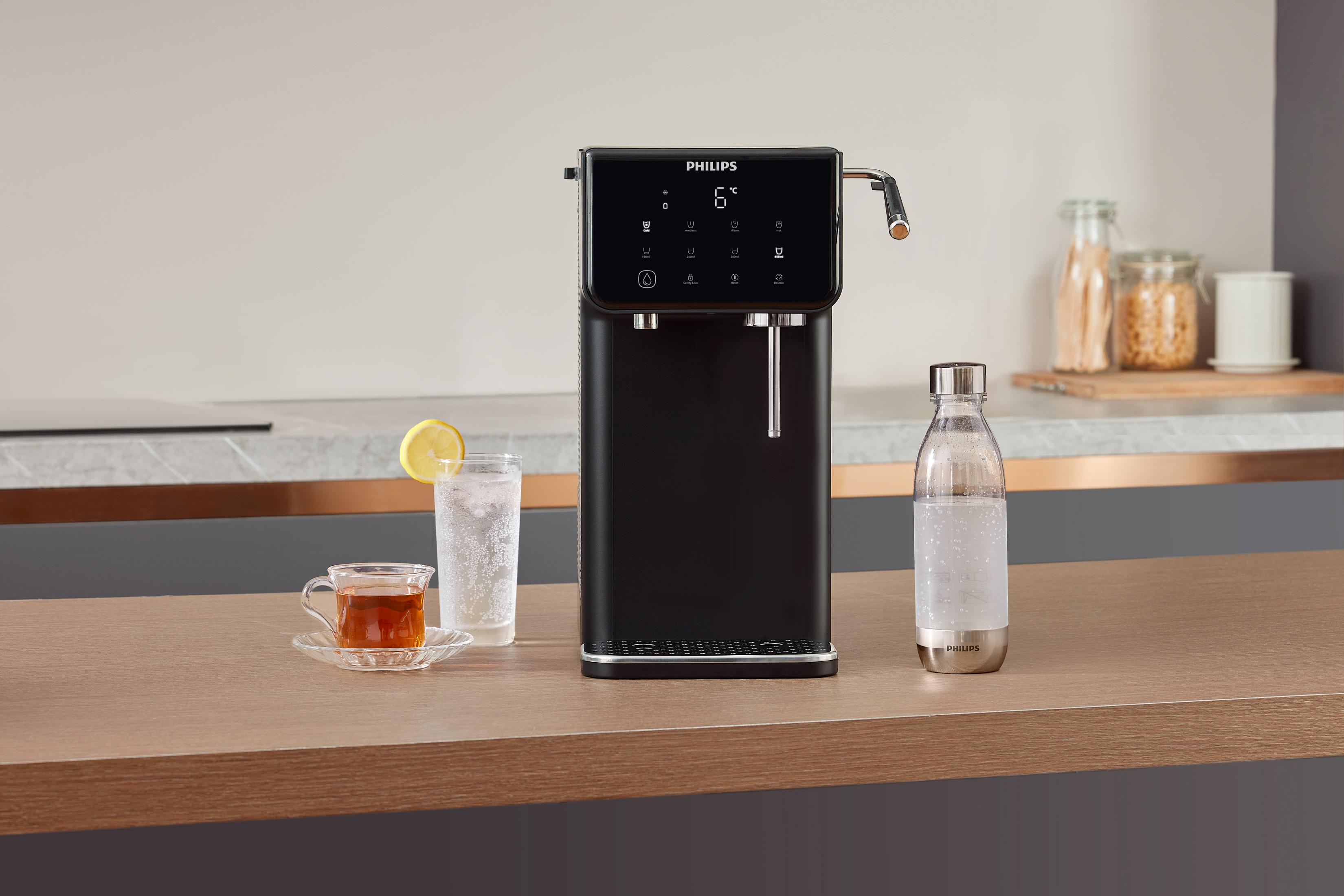 Erogatore d'acqua nero con tè, acqua e limone e bottiglia d'acqua su un piano di legno.