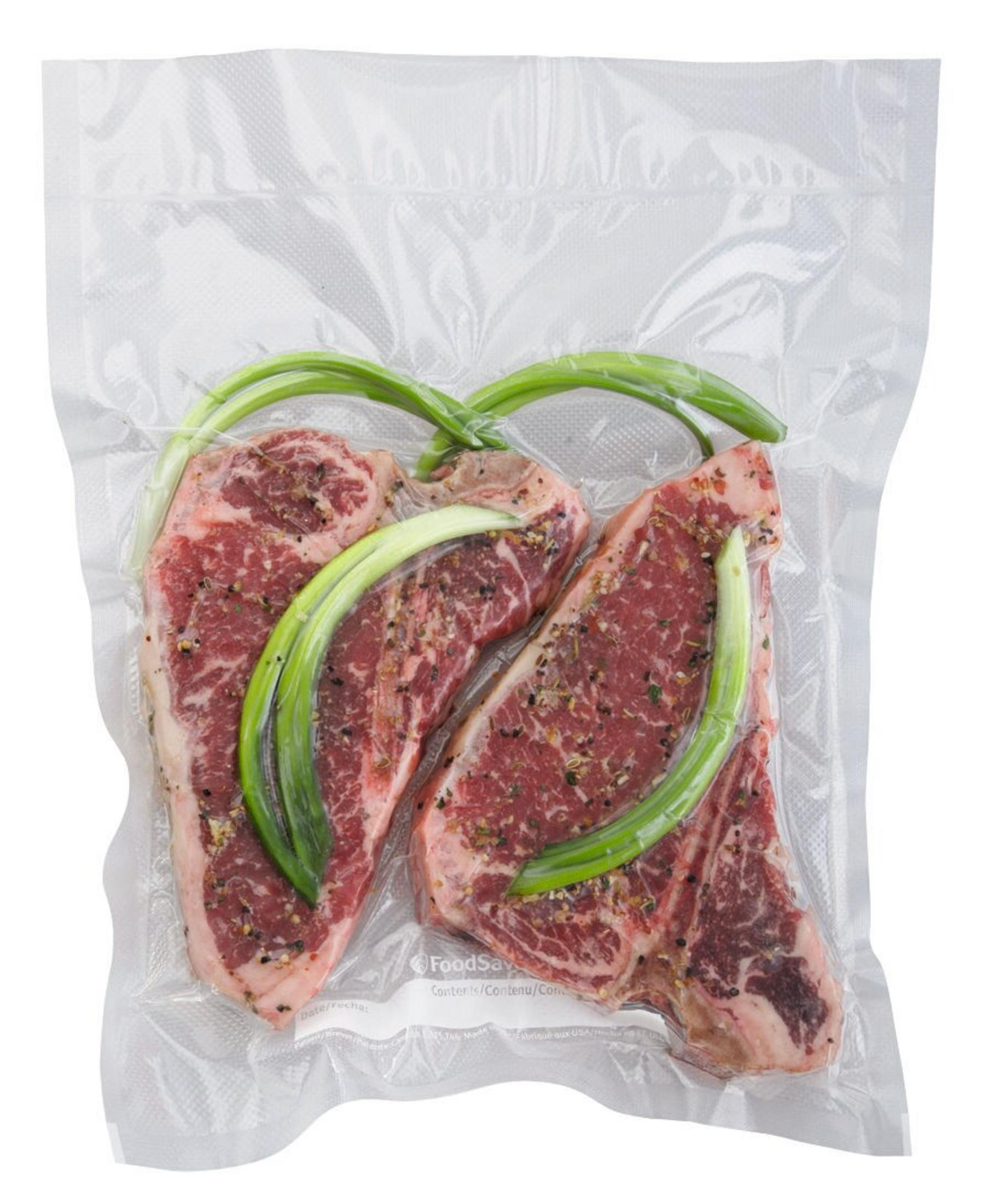 Zwei gewürzte Steaks und grüne Zwiebeln sind in einem durchsichtigen Plastikbeutel vakuumverpackt.