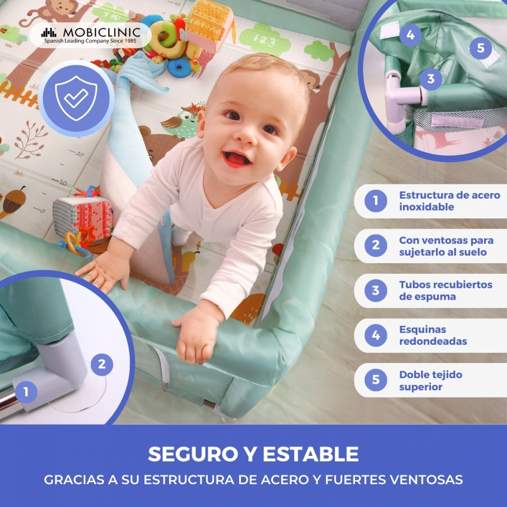 Un bebé sonríe en un parque infantil. Juguetes rodean al bebé, y el parque infantil es de color verde azulado.