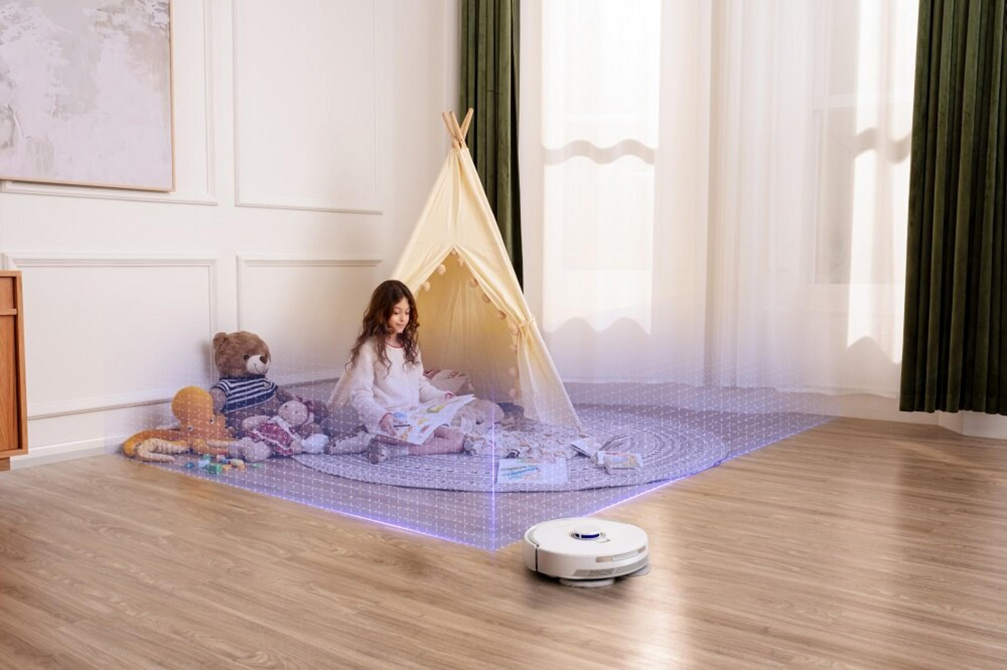 Dziewczynka czyta w tipi. Zabawki i odkurzacz automatyczny są w scenie. Widoczna drewniana podłoga i białe ściany.