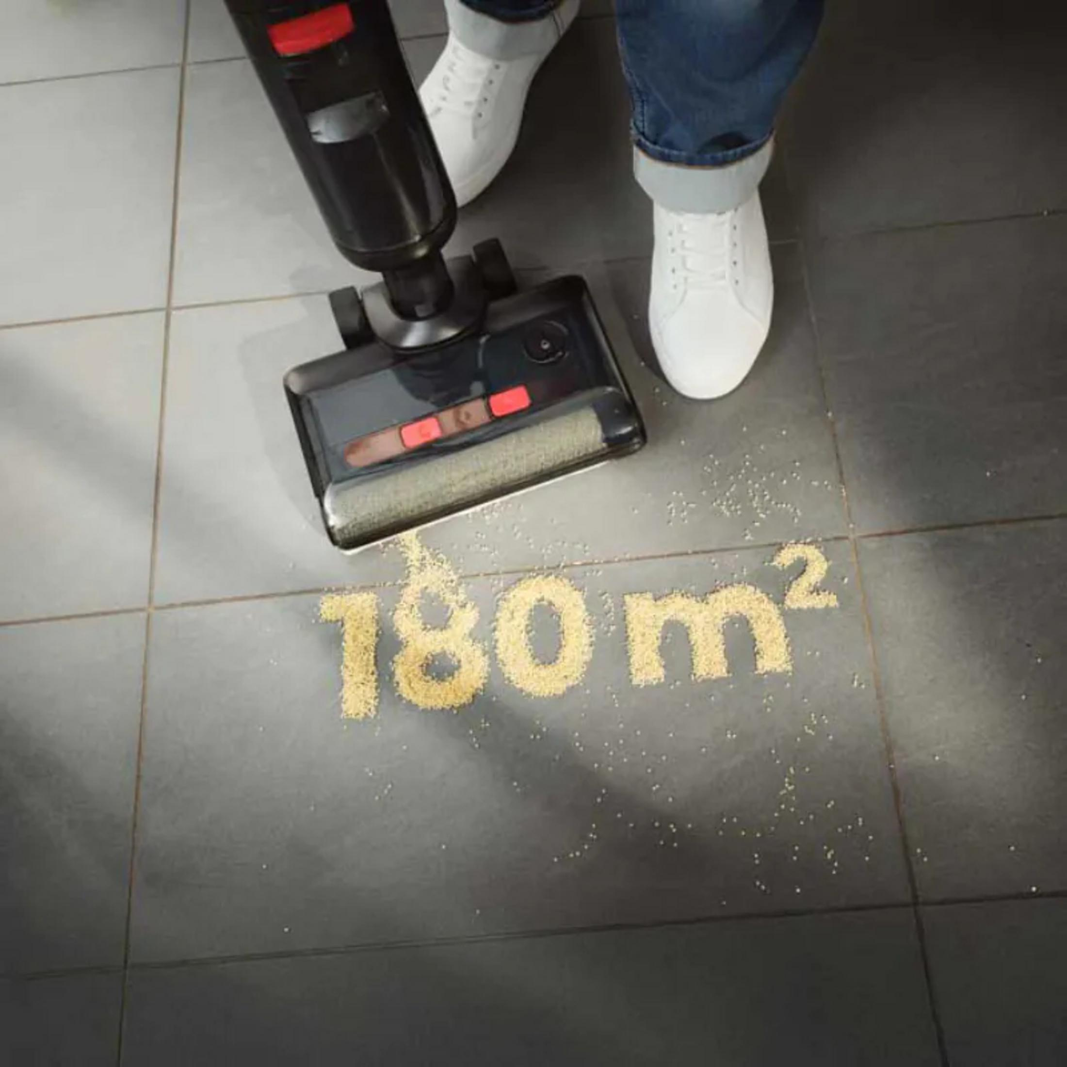 Osoba odkurza podłogę czarnym odkurzaczem. Tekst '180 m²' z małych cząsteczek jest na podłodze.
