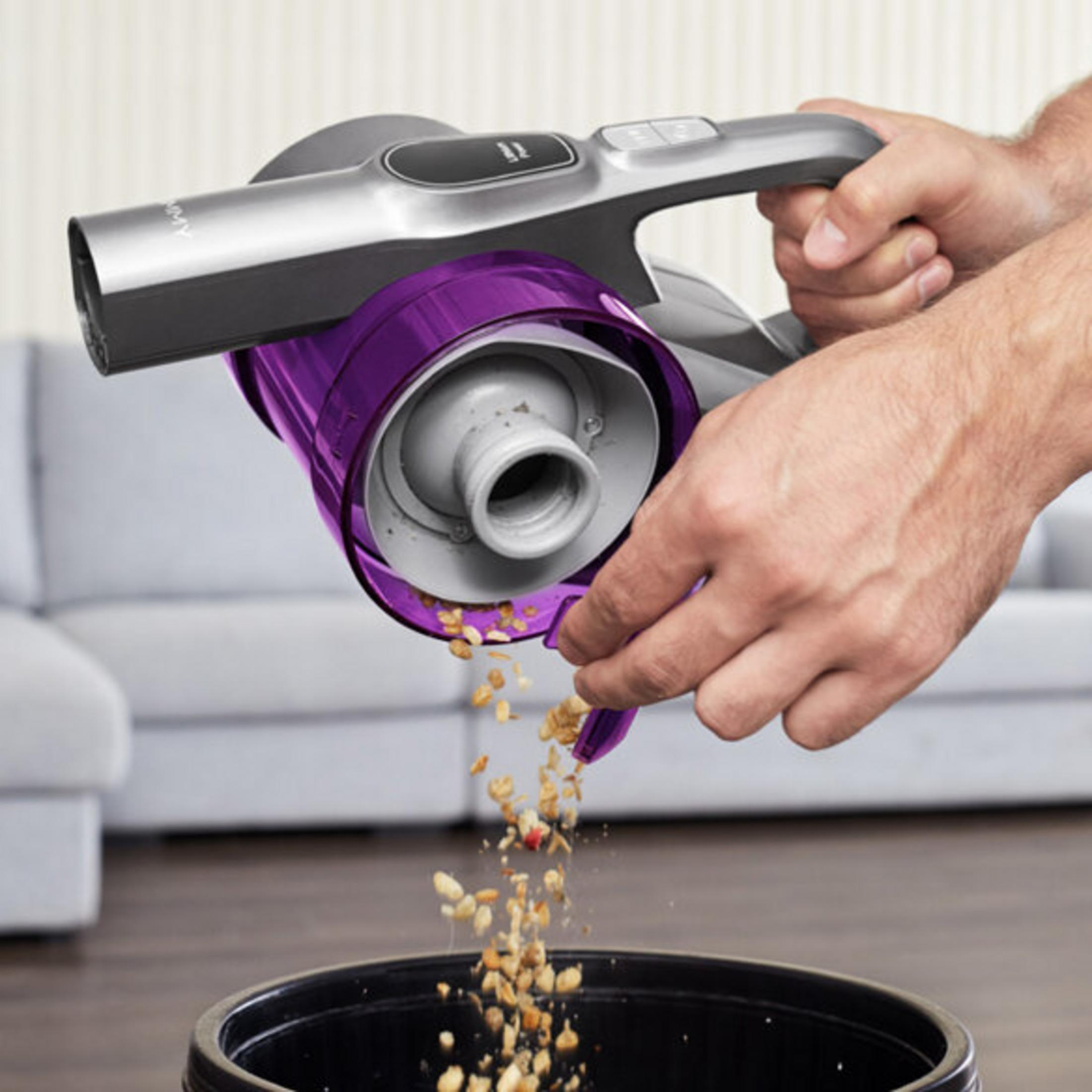 Una persona vacía una aspiradora de mano morada y gris en un cubo negro. Granola cae en el cubo.