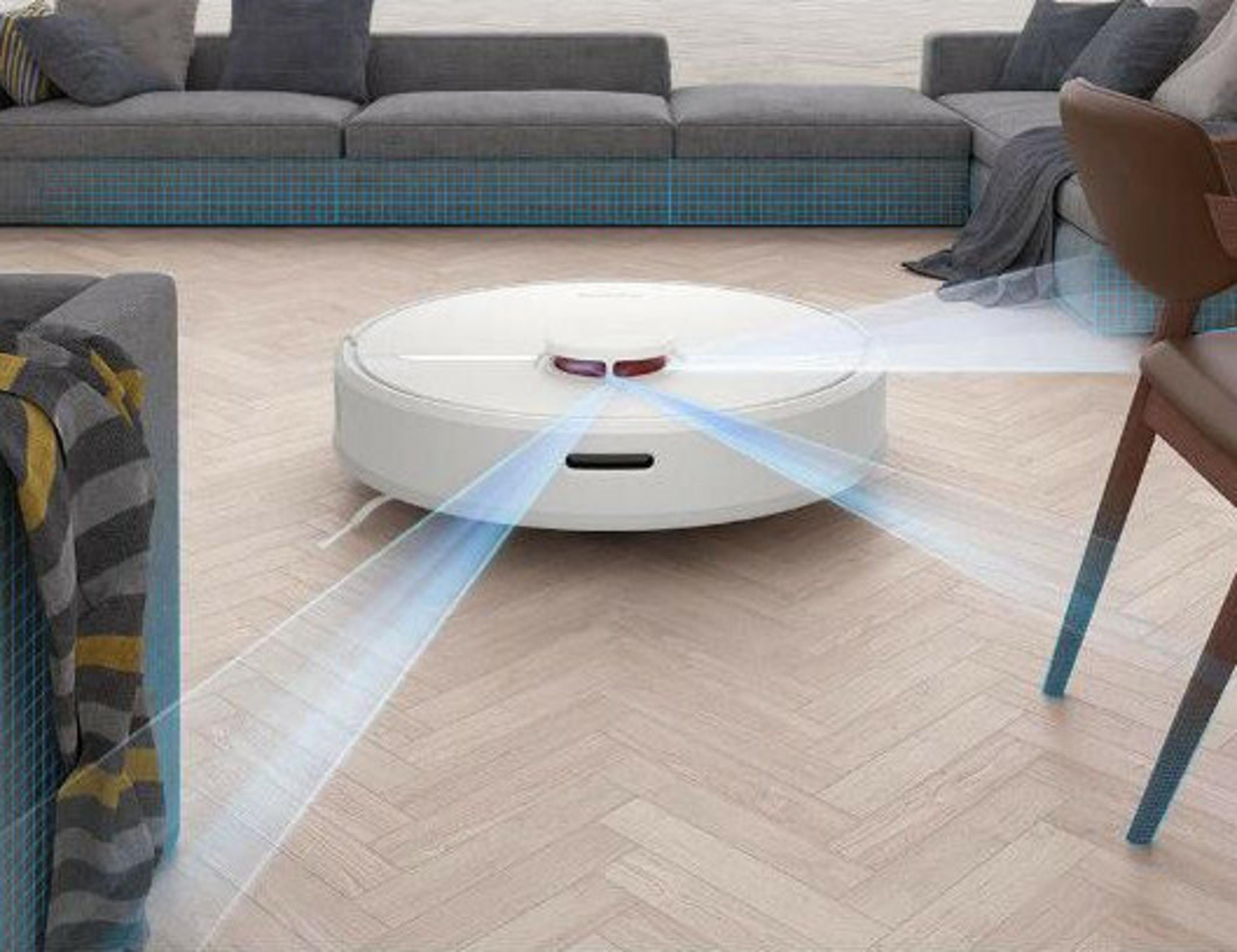Un aspirapolvere robot bianco è su un pavimento in legno. Linee blu mostrano l'area di scansione. Un divano è sullo sfondo.