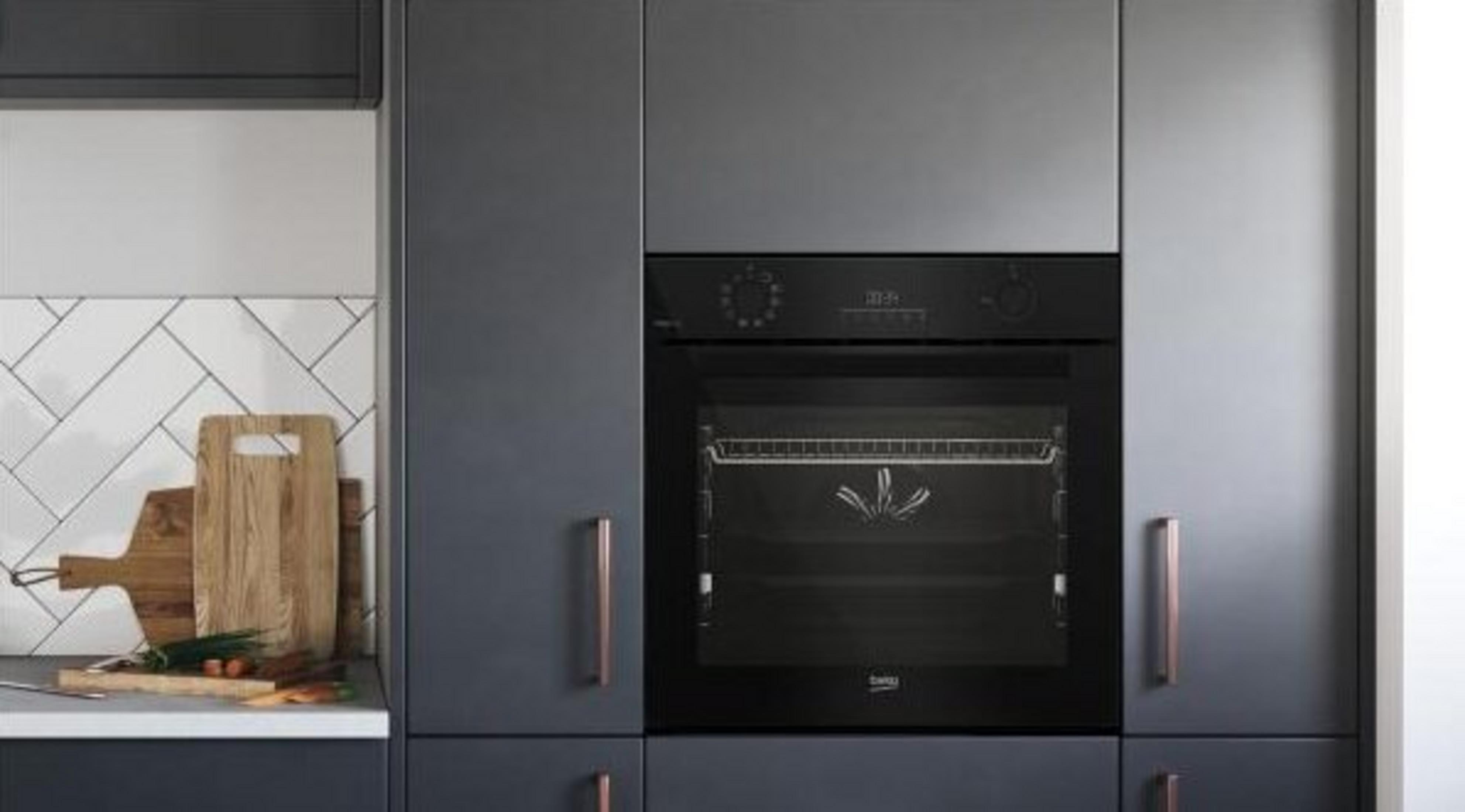 Una cucina moderna con un forno nero al centro. Taglieri e verdure sono sul bancone a sinistra.