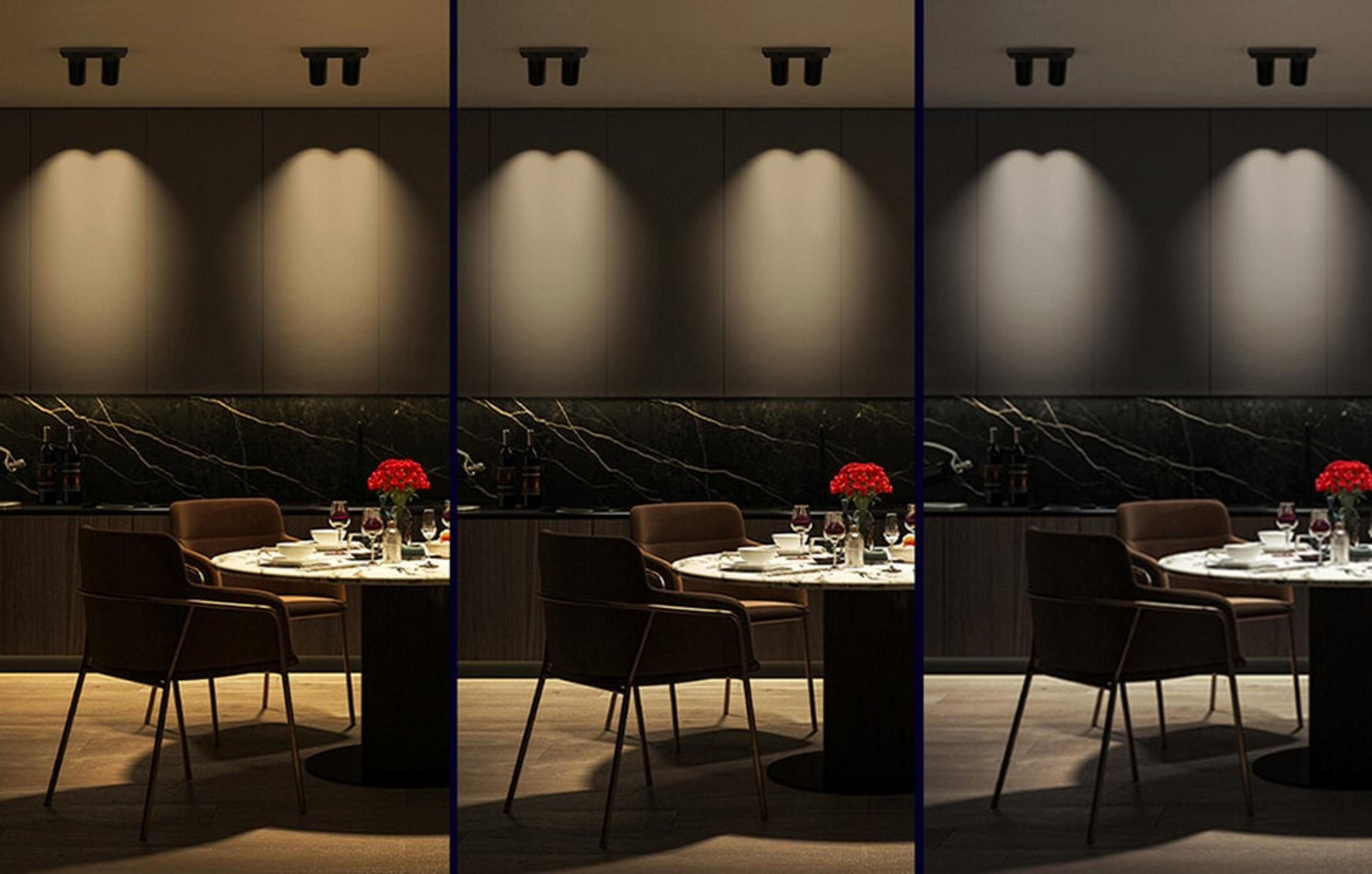 Scena jadalni z okrągłym stołem, krzesłami, kwiatami i oświetleniem. Widoczne szafki kuchenne i marmurowa ściana.