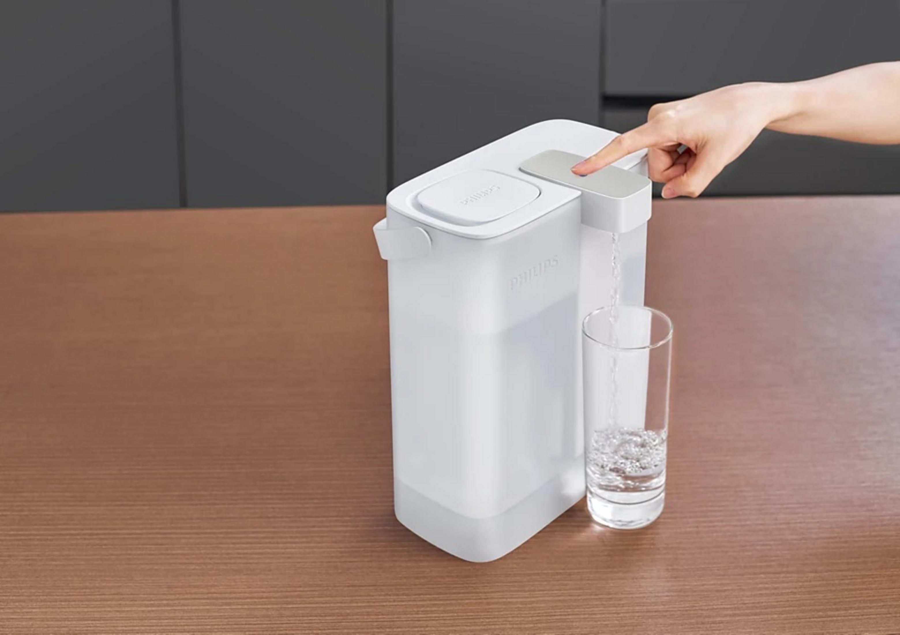 Een witte Philips waterdispenser schenkt water in een glas op een bruin aanrecht. Een hand drukt op een knop.