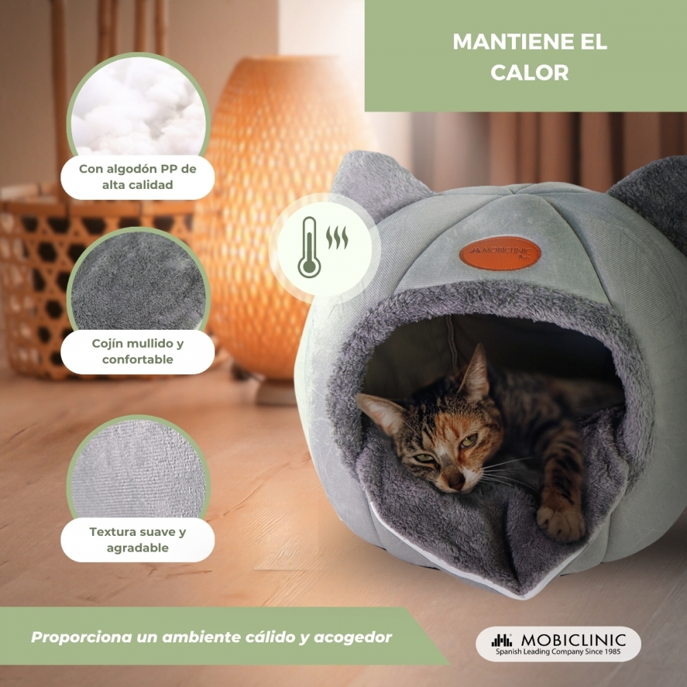 Un gato descansa en una cama gris para gatos. La cama tiene un interior suave. El texto menciona algodón de alta calidad y un ambiente cálido.