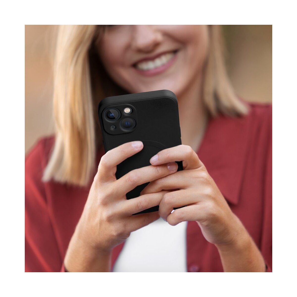 Eine Frau hält ein schwarzes Telefon und lächelt. Sie trägt ein rotes Hemd. Das Telefon hat eine Hülle. Blondes Haar ist sichtbar.
