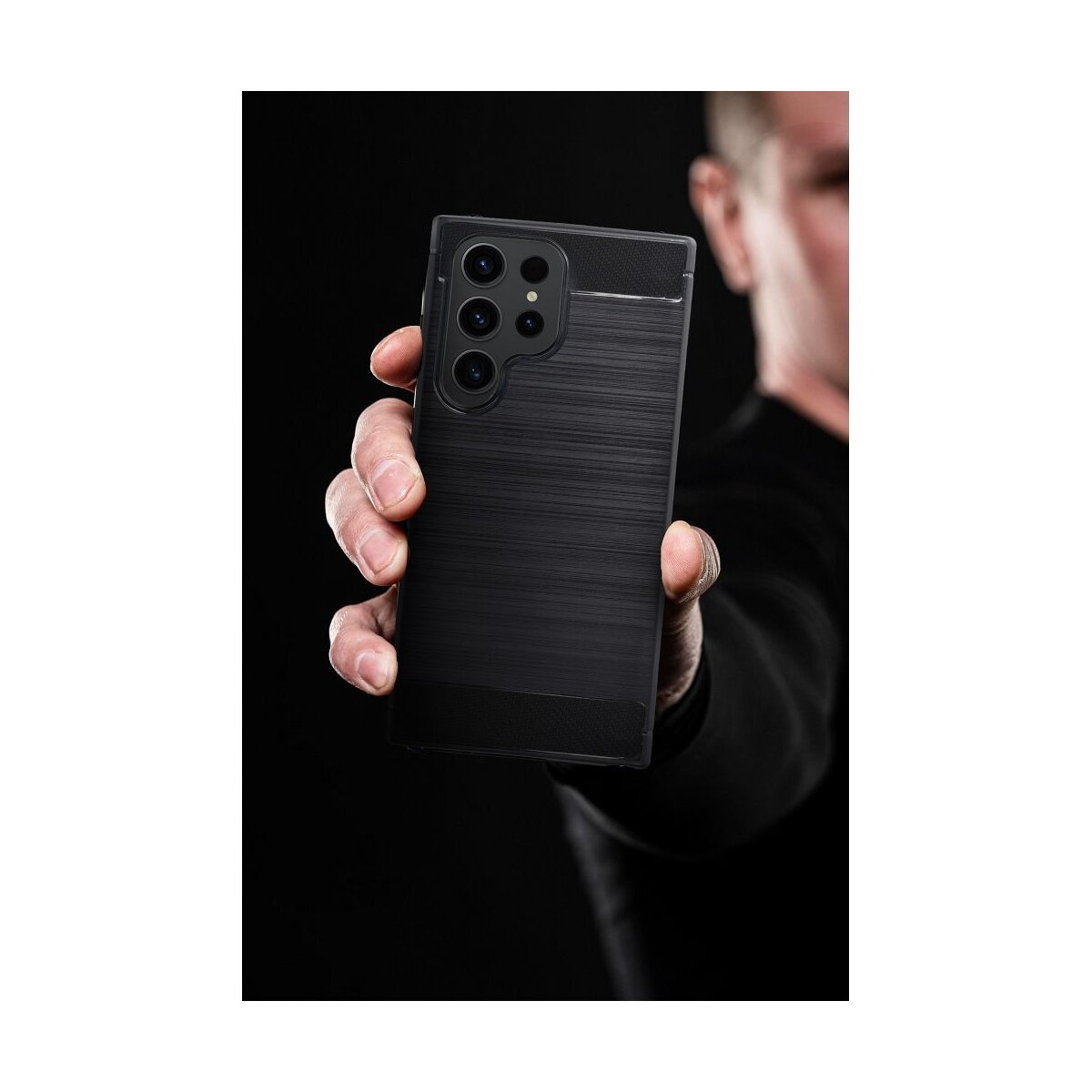 Eine Person hält ein schwarzes Smartphone mit mehreren Kameras. Das Telefon hat eine strukturierte Rückseite. Dunkler Hintergrund.