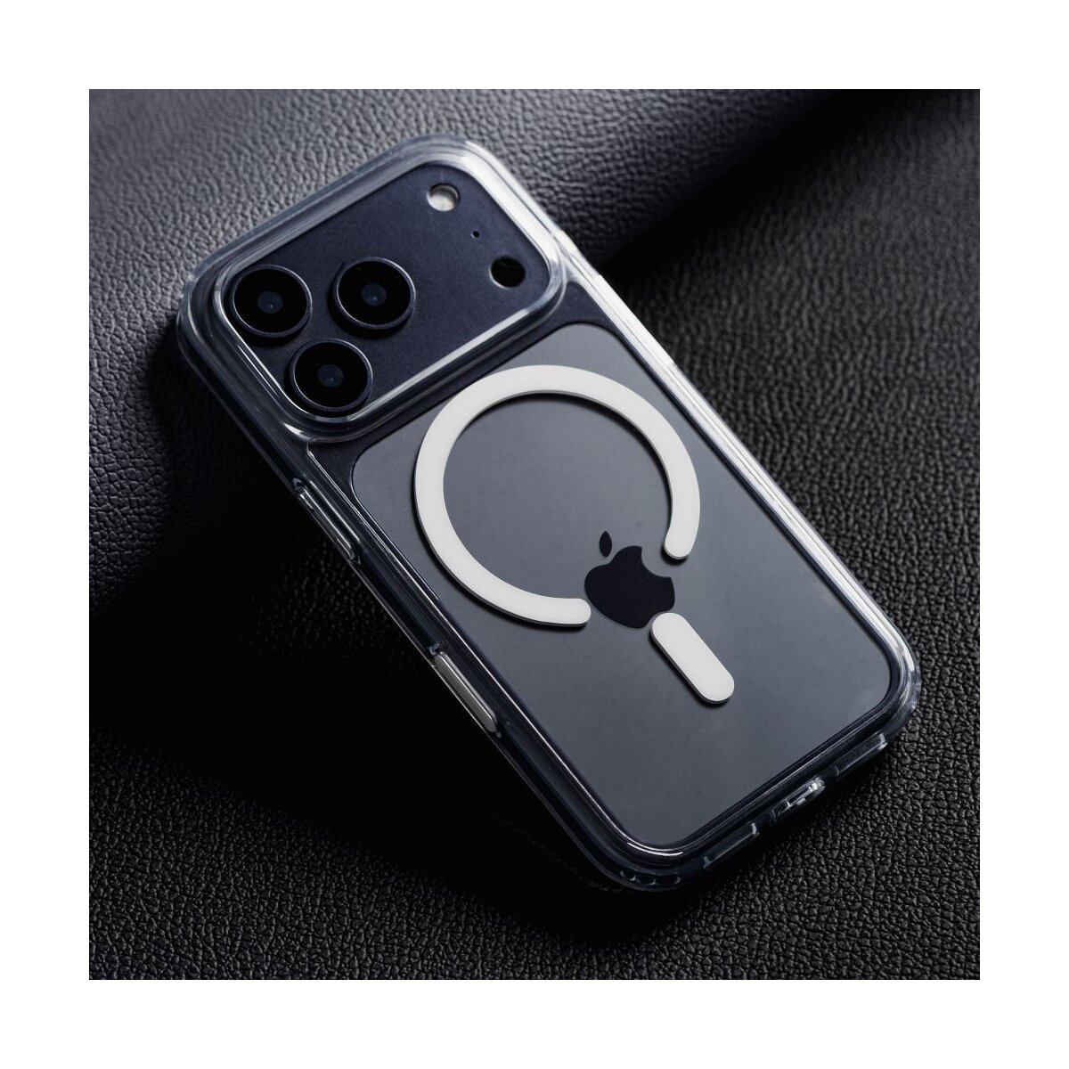 Transparente iPhone-Hülle mit weißem MagSafe-Ring und Apple-Logo auf dunkler Lederoberfläche. Die Hülle hat drei Kameralinsen.
