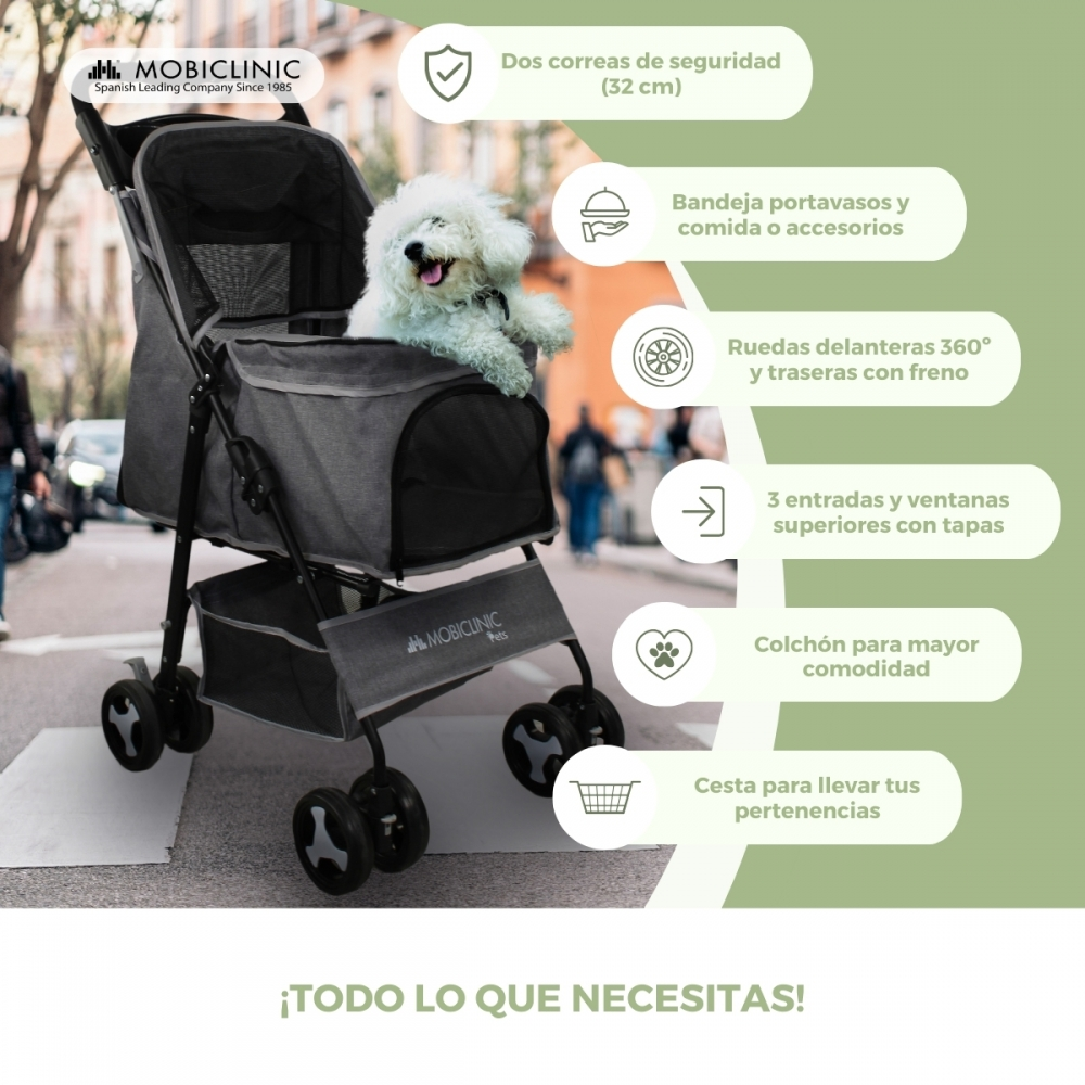 Un perro blanco sentado en un cochecito gris oscuro para mascotas en una calle de la ciudad. El cochecito tiene cesta y características.