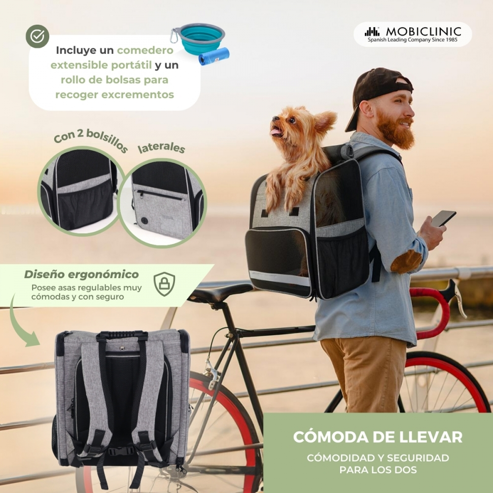 Un hombre lleva un perro en una mochila en una bicicleta. La mochila tiene un diseño gris y negro. Incluye un cuenco portátil y bolsas.