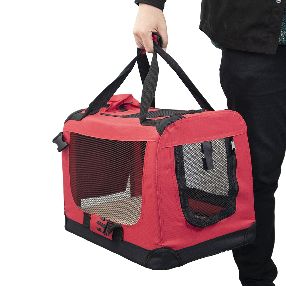 Una persona sostiene un transportín rojo y negro. El transportín tiene ventanas de malla y asas negras. La persona lleva pantalones y una chaqueta negros.
