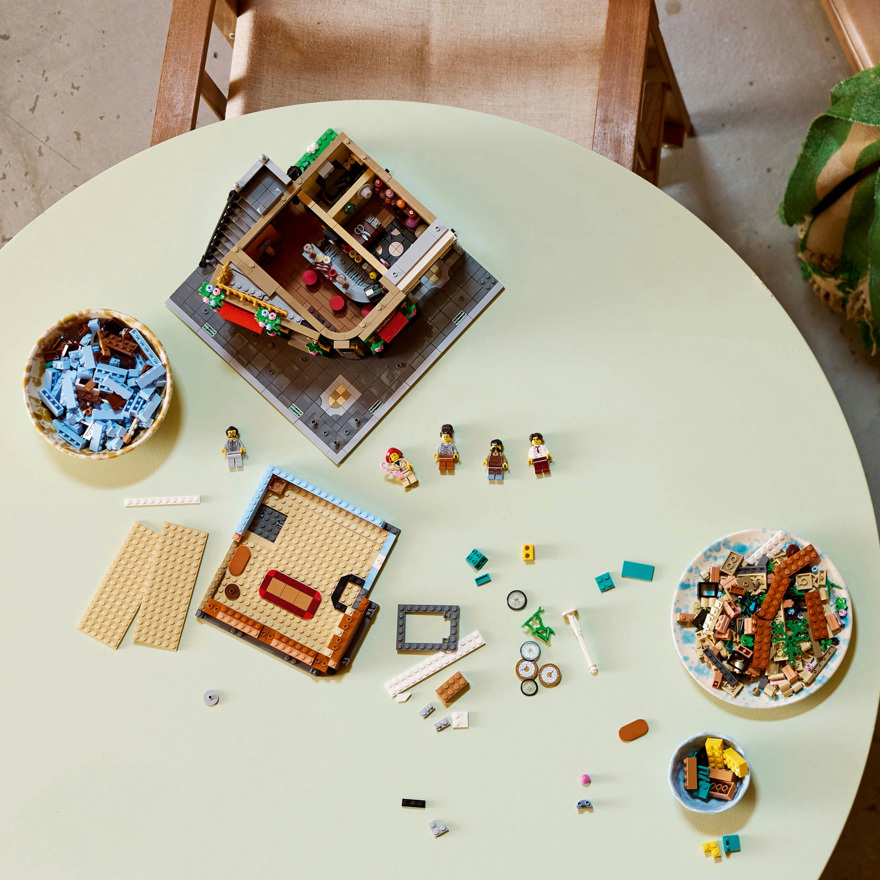 Lego-Set auf einem Tisch, teilweise aufgebaut. Enthält Schalen mit Steinen, Minifiguren und Bauteilen.