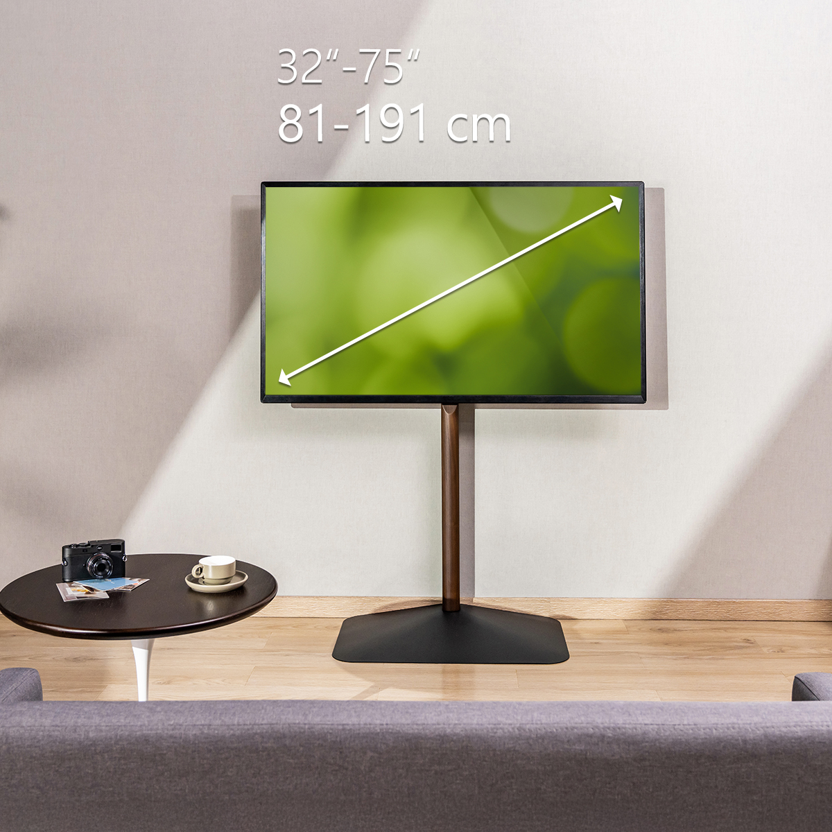 Fernseher auf Ständer, Couchtisch mit Tasse und Kamera. Graues Sofa davor. Text zeigt Bildschirmgröße.