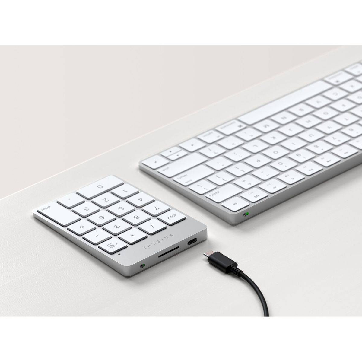 Un teclado blanco y un teclado numérico están sobre una superficie blanca. Un cable USB-C negro conecta el teclado numérico.