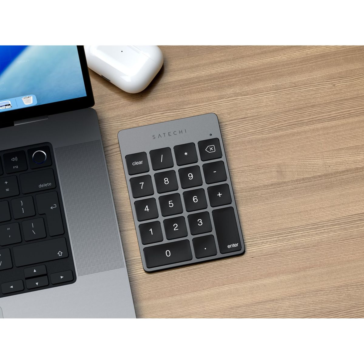 Ein graues Ziffernfeld mit schwarzen Tasten liegt auf einem Holztisch neben einem Laptop und einem weißen Kopfhörergehäuse.
