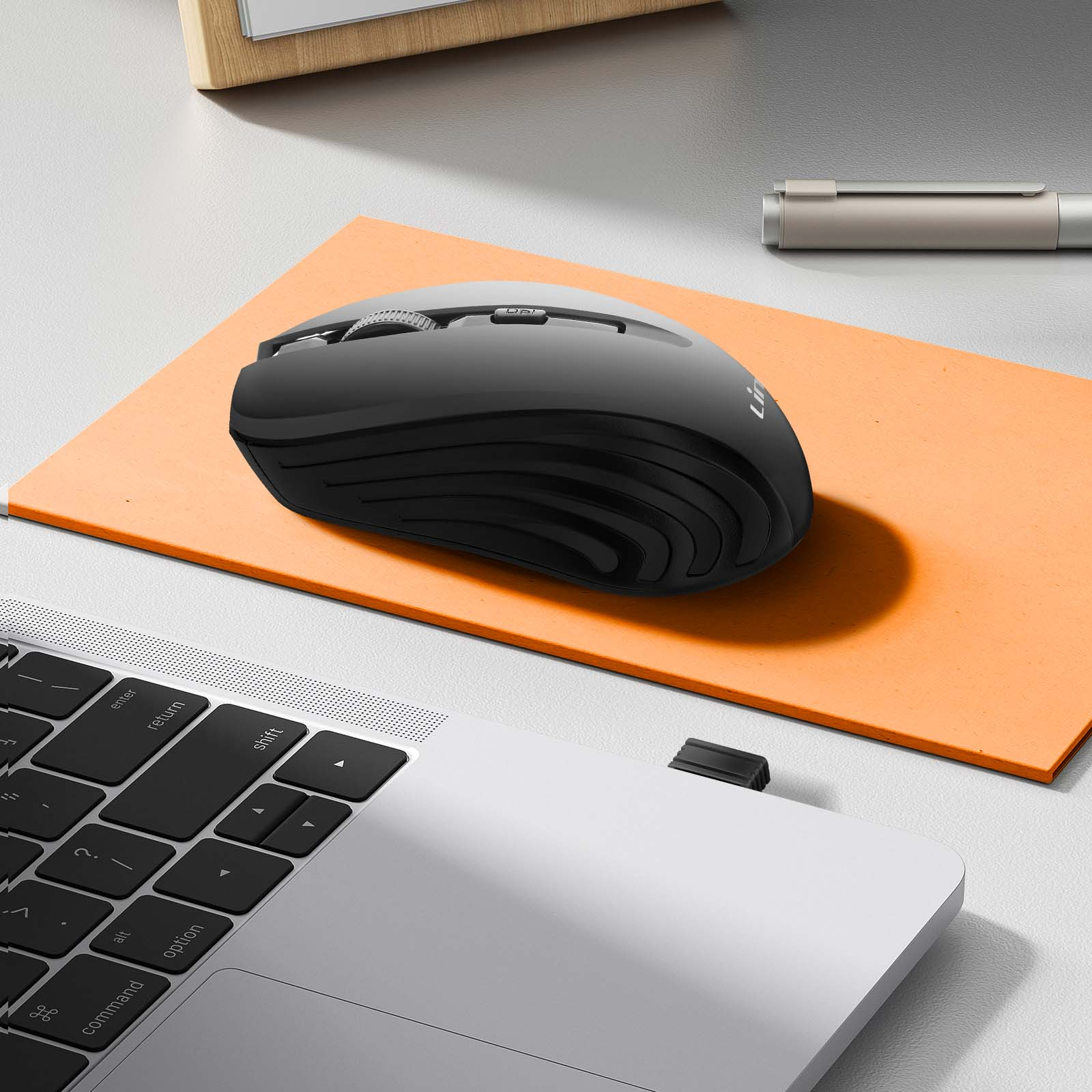 Un mouse wireless nero è su un tappetino arancione, vicino a una tastiera di un laptop. Una penna sullo sfondo.