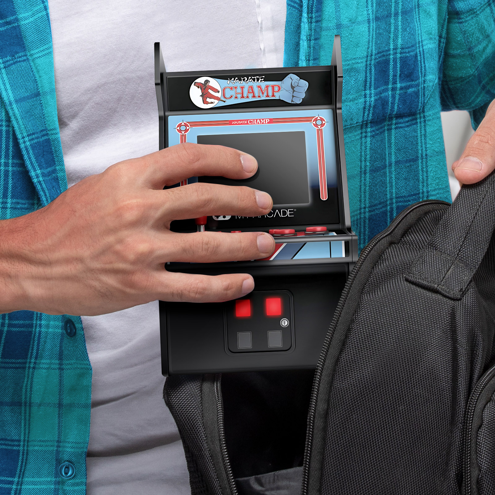 Una persona sostiene un minijuego arcade titulado Karate Champ. El juego es negro con una pantalla y botones rojos. Está en una bolsa negra.