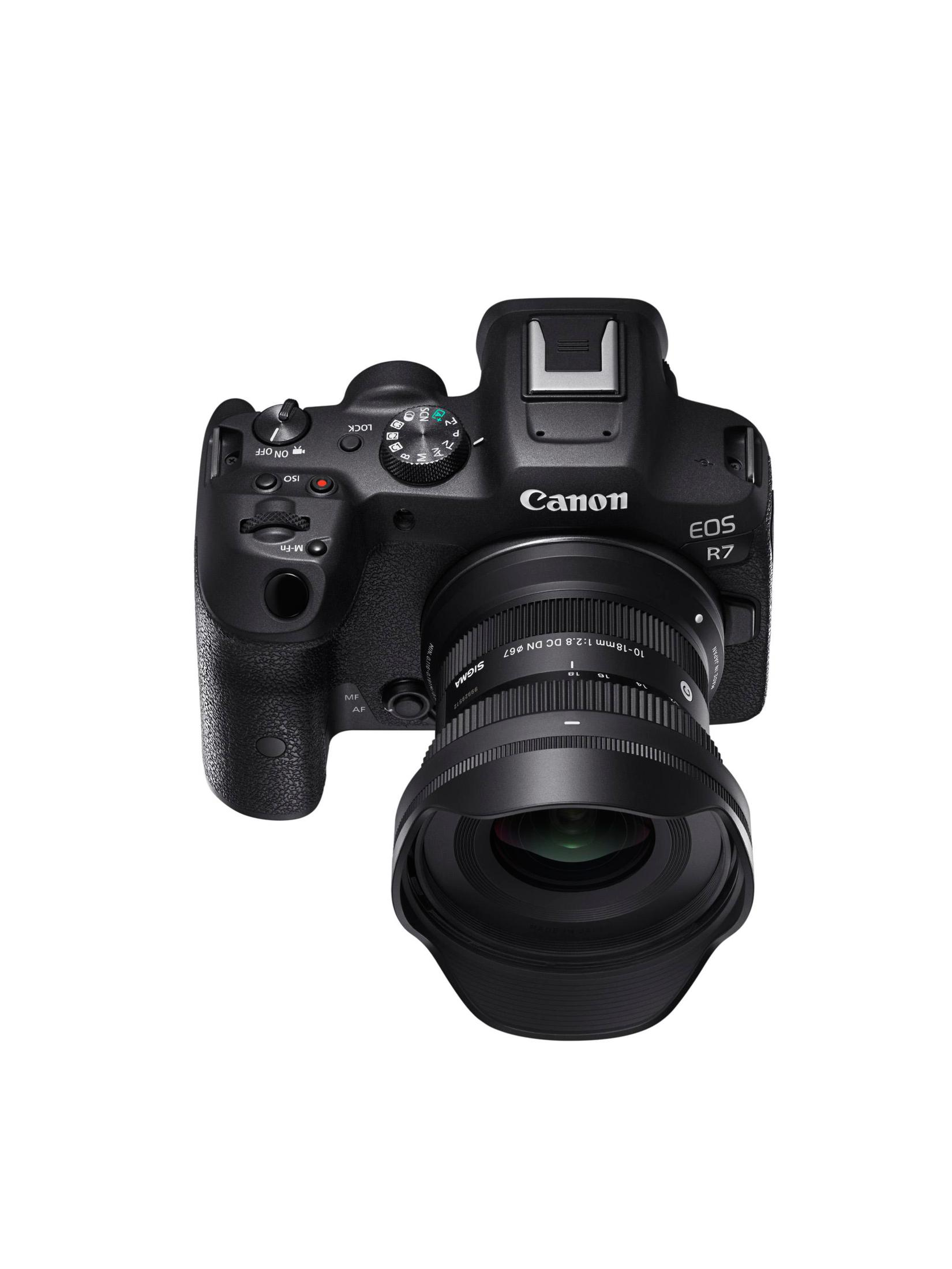 Fotocamera Canon EOS R7 nera con obiettivo Sigma. La fotocamera è su sfondo bianco. L'obiettivo è 10-18mm 1:2.8 DC DN.