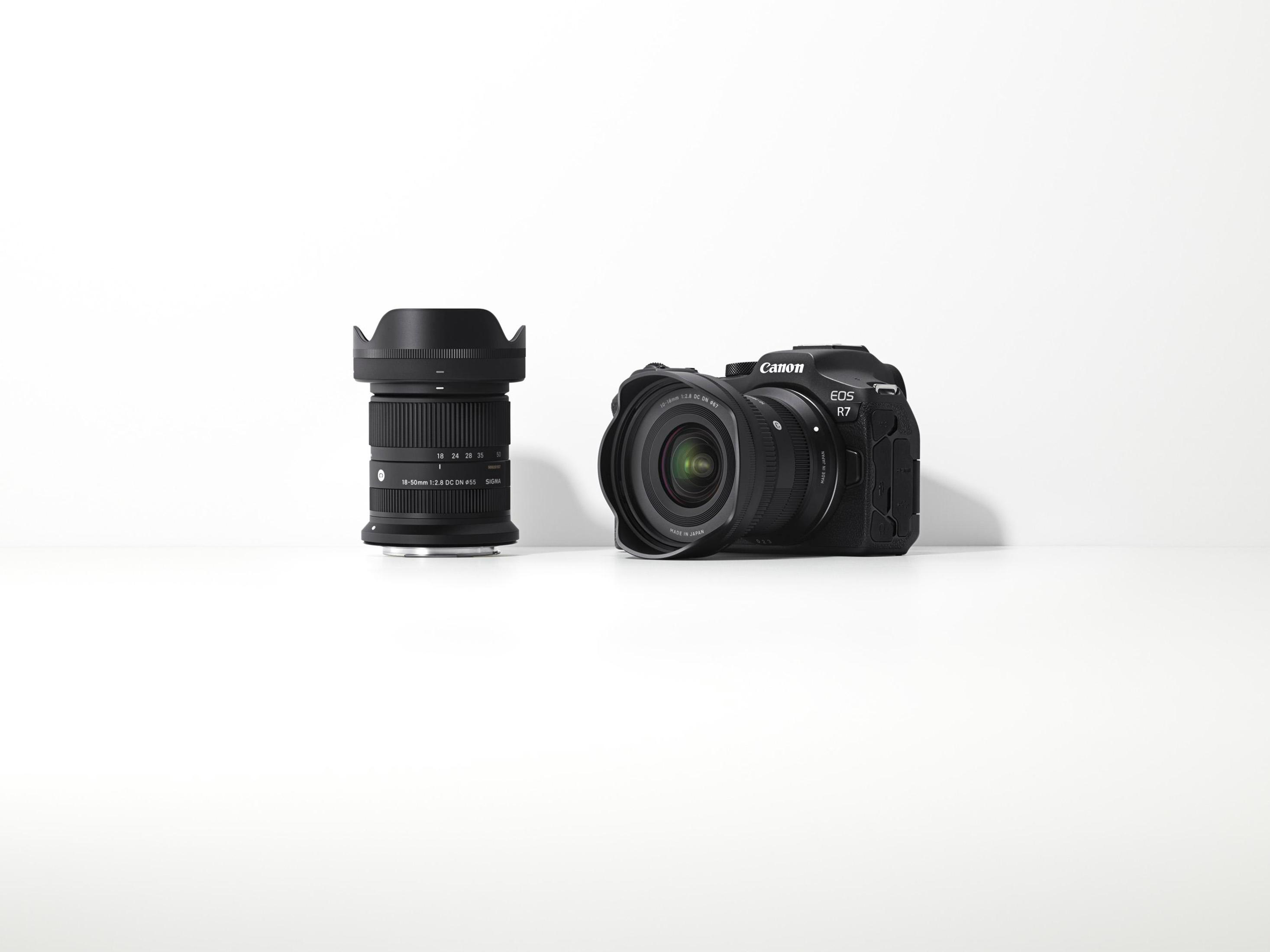 Una fotocamera Canon EOS R7 e un obiettivo Sigma su una superficie bianca. Entrambi sono neri.