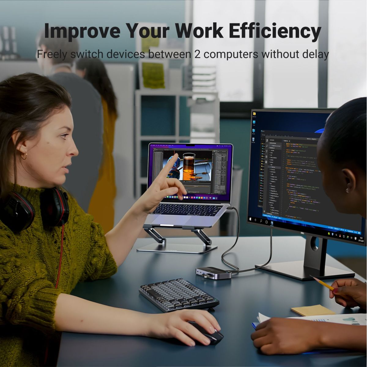 Kobieta wskazuje na ekran laptopa podłączonego do monitora. Klawiatura i mysz na biurku. Inna osoba przy monitorze.