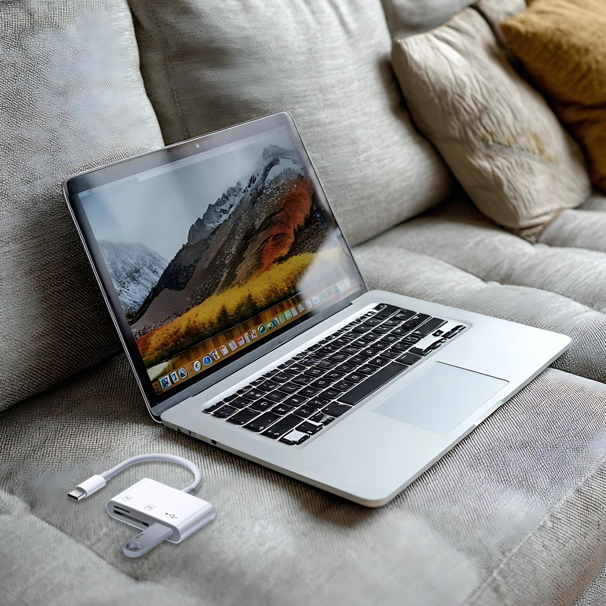 Laptop auf einer Couch mit einer Berglandschaft auf dem Bildschirm. Vorne ein weißer Adapter mit USB-C und USB-Stick.