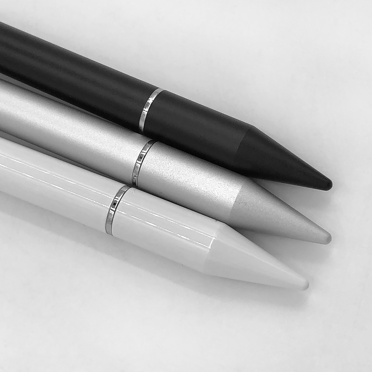 Trzy rysiki, czarny, srebrny i biały, leżą ukośnie na białej powierzchni. Każdy ma metalowy srebrny pasek i zwężającą się końcówkę.