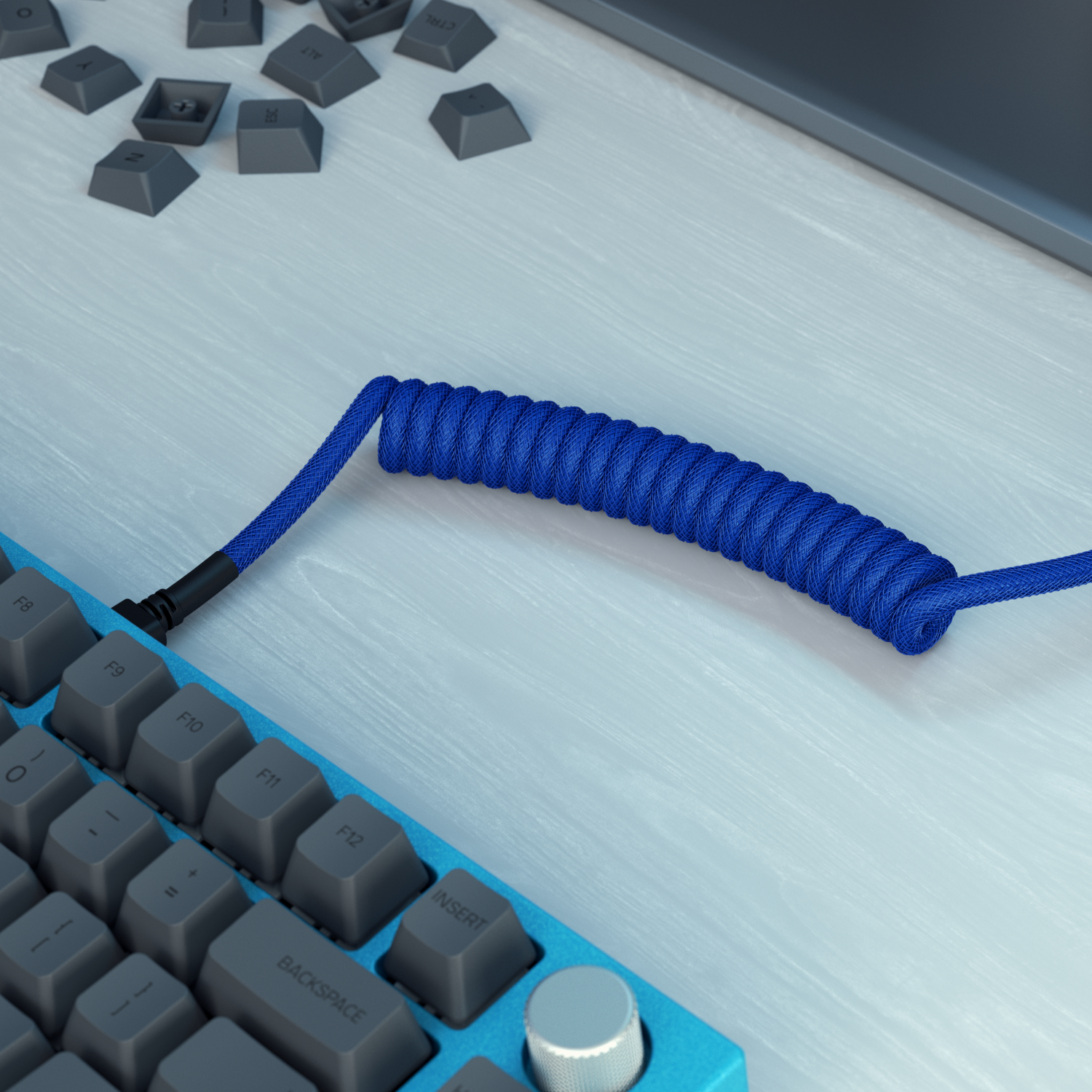 Un cavo blu a spirale per tastiera, tasti e tasti staccati su una superficie di venature chiare, con una tastiera blu.