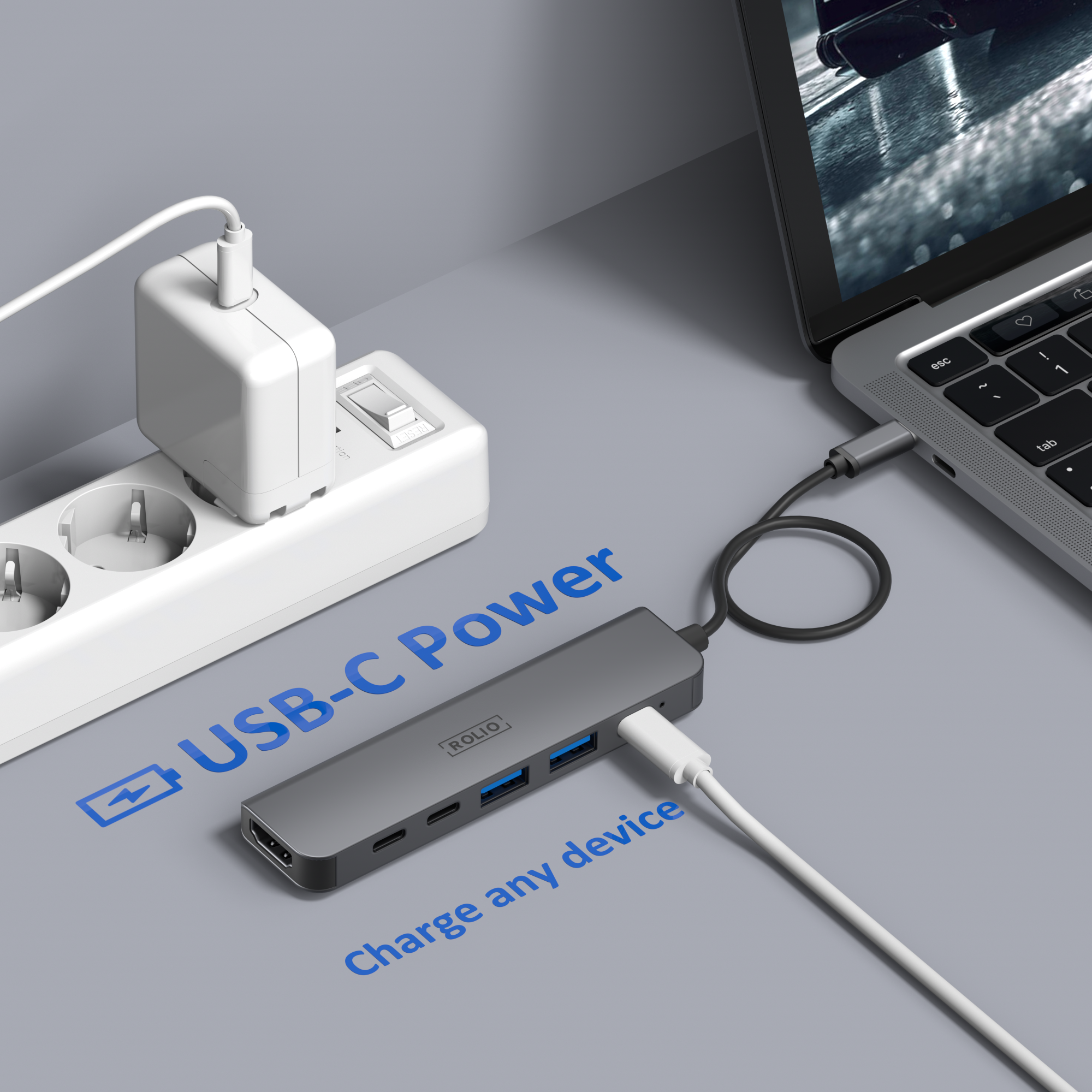 A laptop is connected to a gray USB-C hub. A white power adapter is plugged into a power strip.