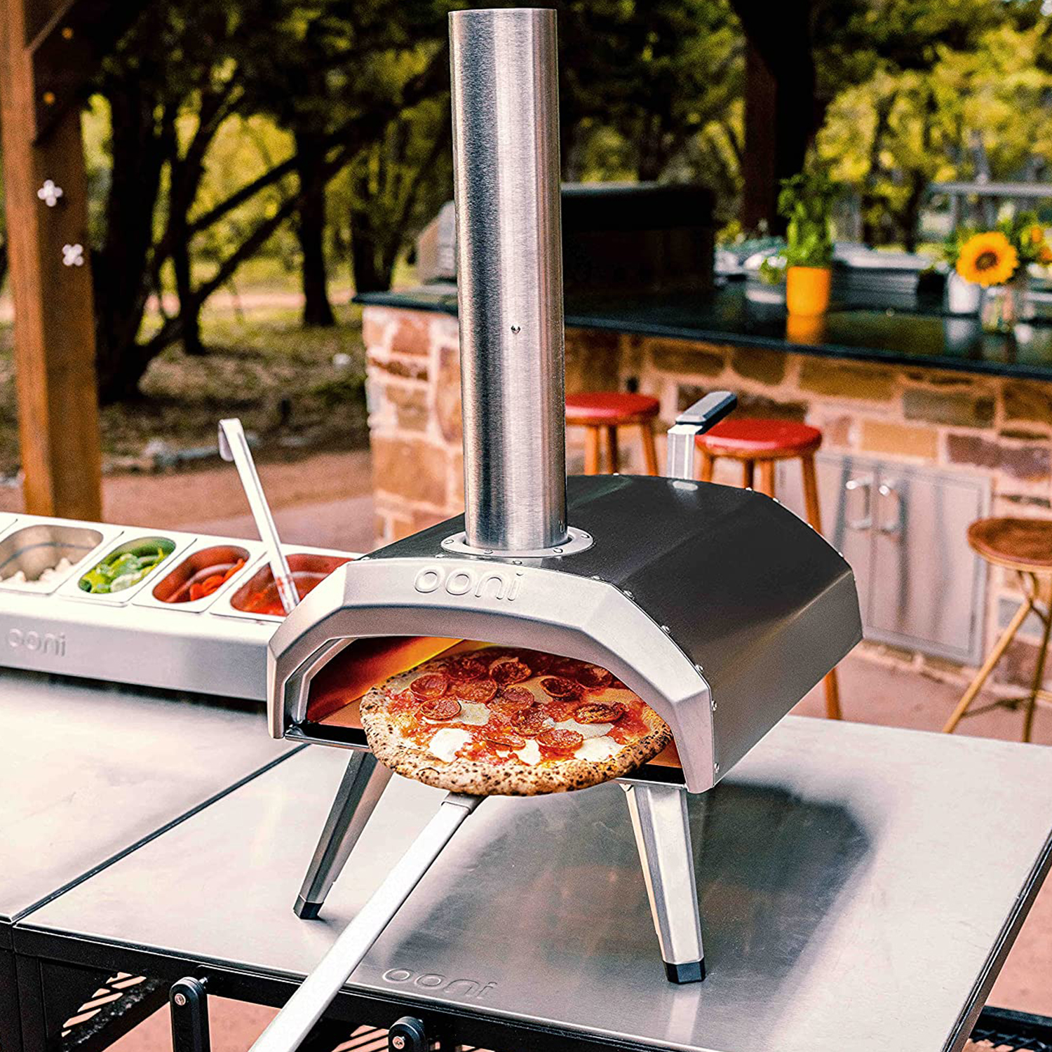 Una pizza è in un forno all'aperto. Una persona usa una pala per togliere la pizza. Ci sono condimenti e ingredienti.