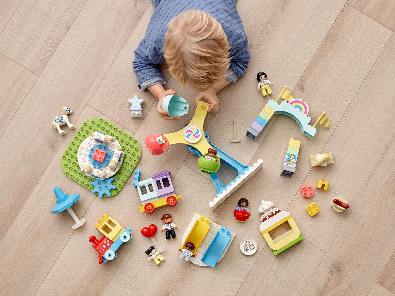 Ein Kind spielt mit bunten Spielzeugstrukturen auf einem Holzboden. Es gibt Spielfiguren und einen Zug.