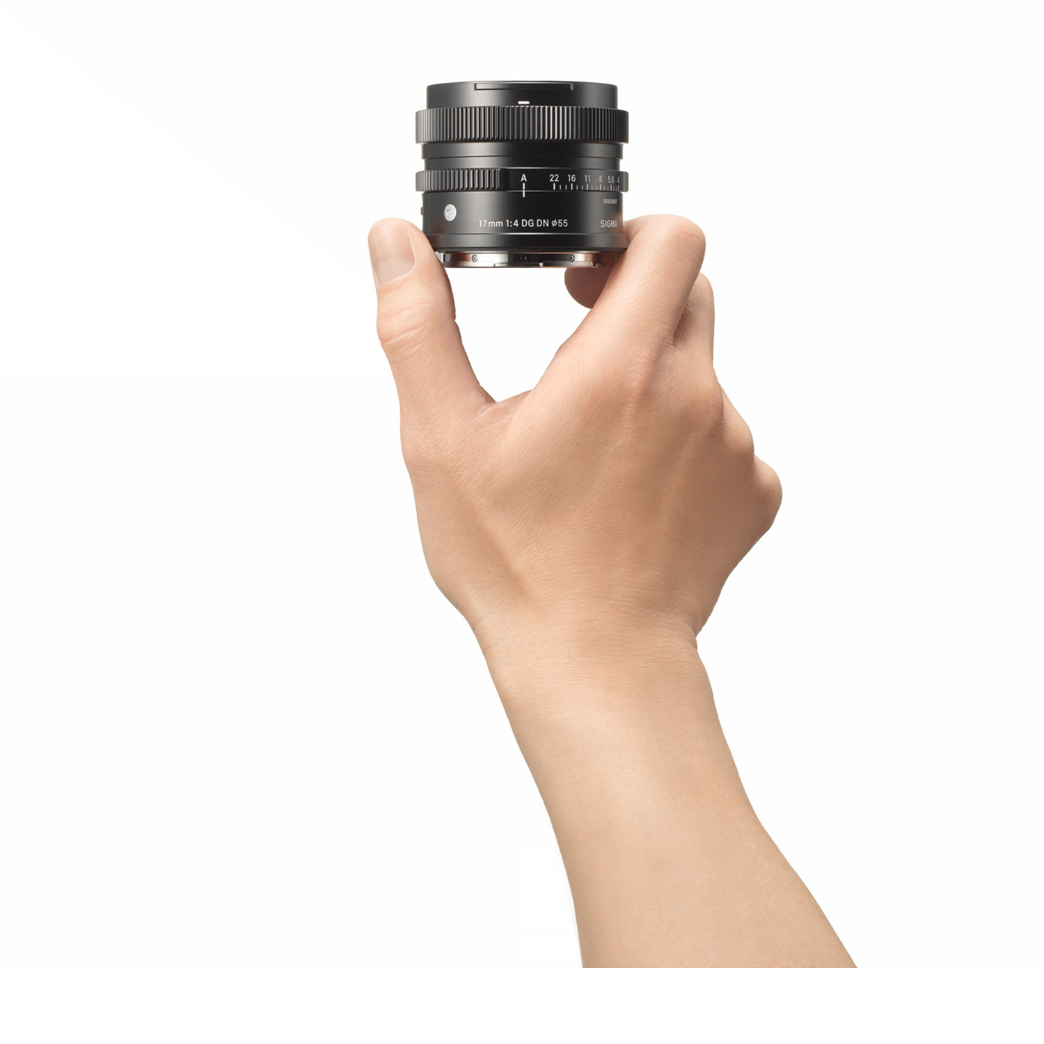 Una mano tiene un obiettivo nero per fotocamera su sfondo bianco. L'obiettivo è etichettato '17mm 1:4 DG DN φ55 SIGMA'.