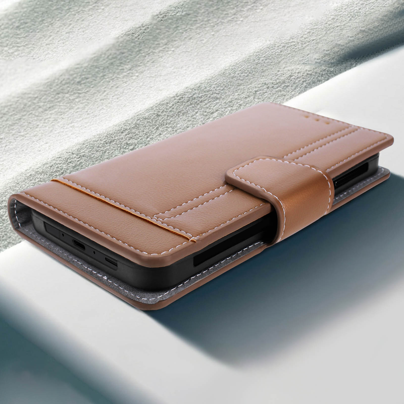 Una custodia per telefono in pelle marrone è aperta. Ha cuciture bianche e una chiusura magnetica. Lo sfondo è una superficie bianca.
