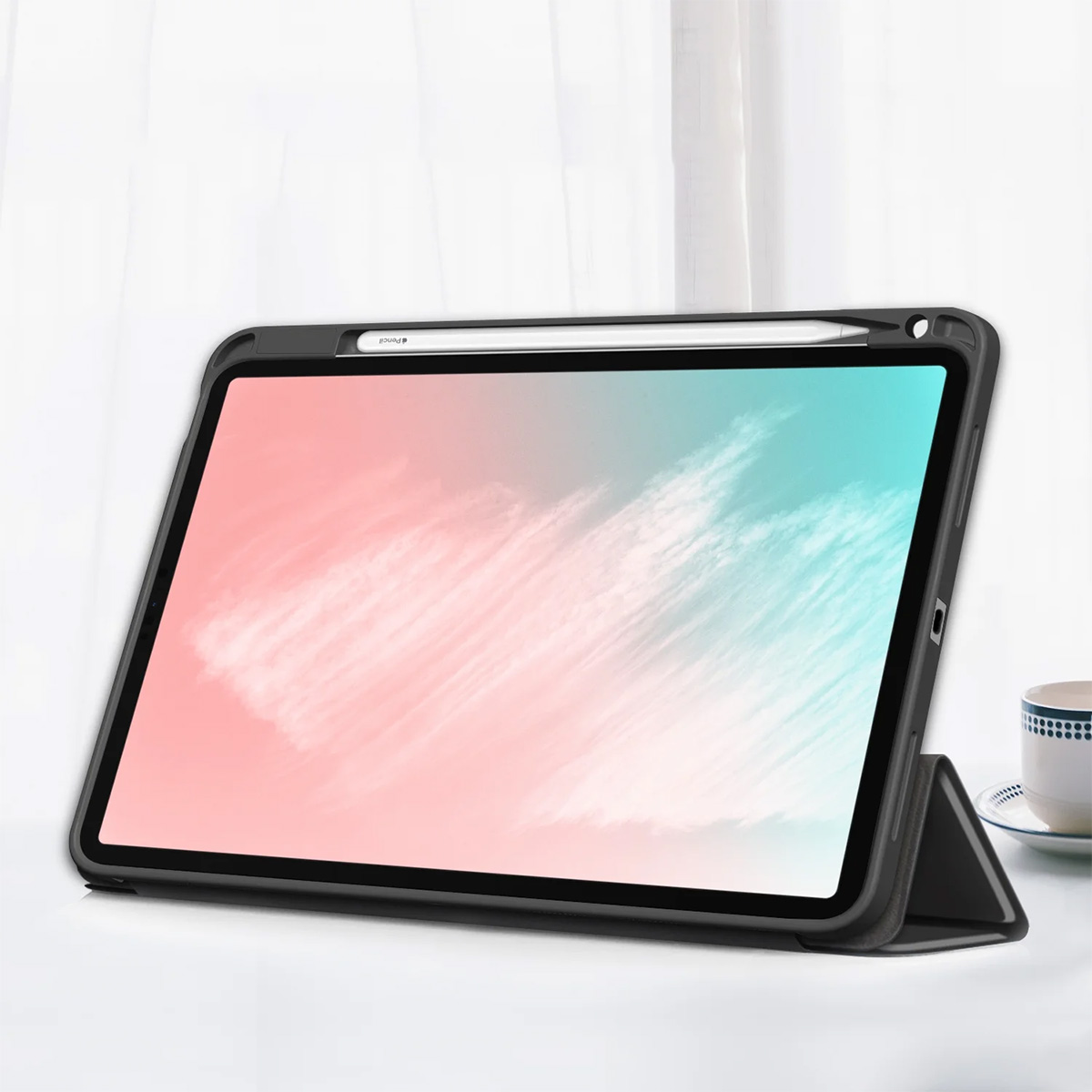 Tablet in custodia nera, con stilo, su tavolo bianco. Schermo mostra tonalità rosa e blu. Tazza a destra.