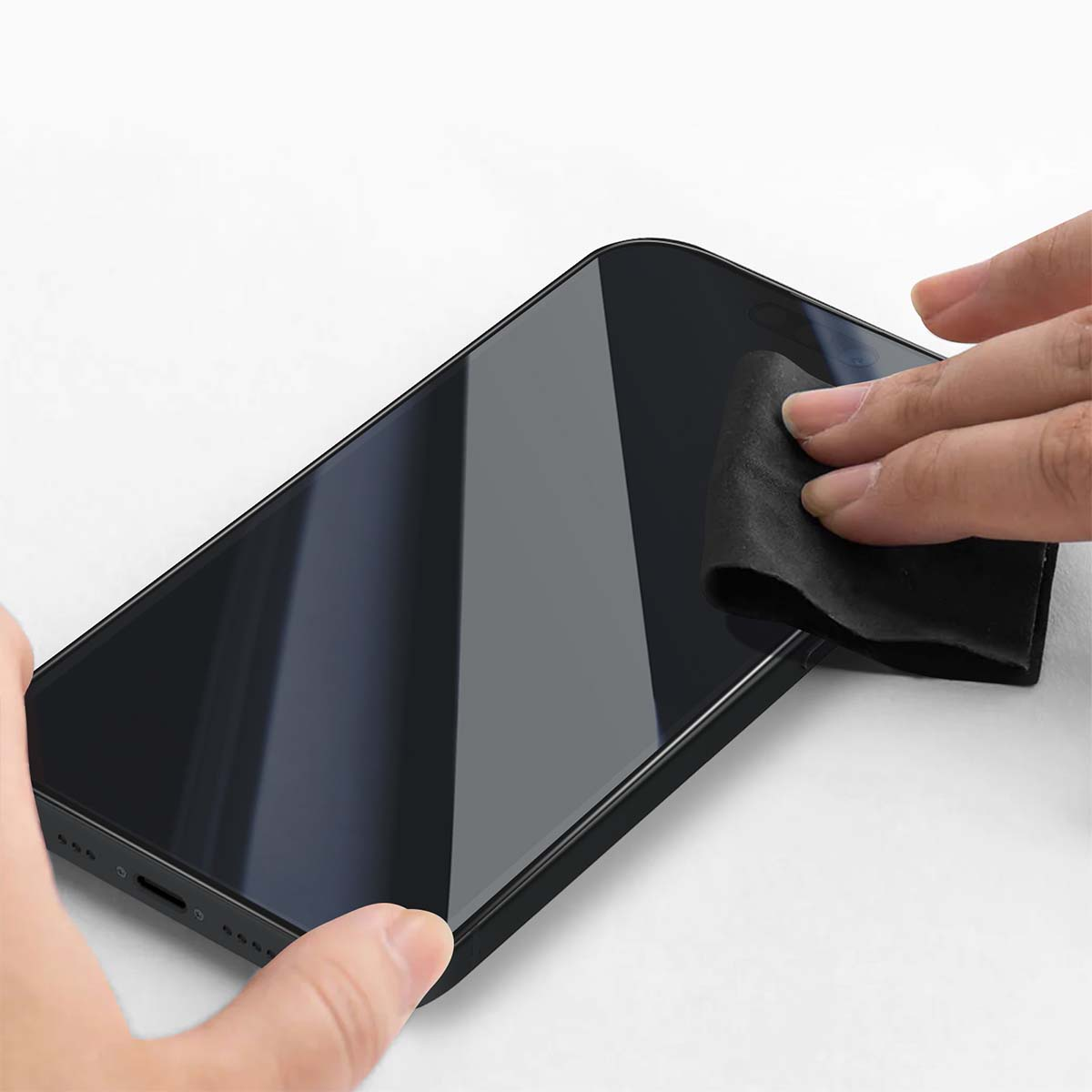 Una mano pulisce lo schermo nero di uno smartphone con un panno nero. Il telefono è su una superficie bianca.