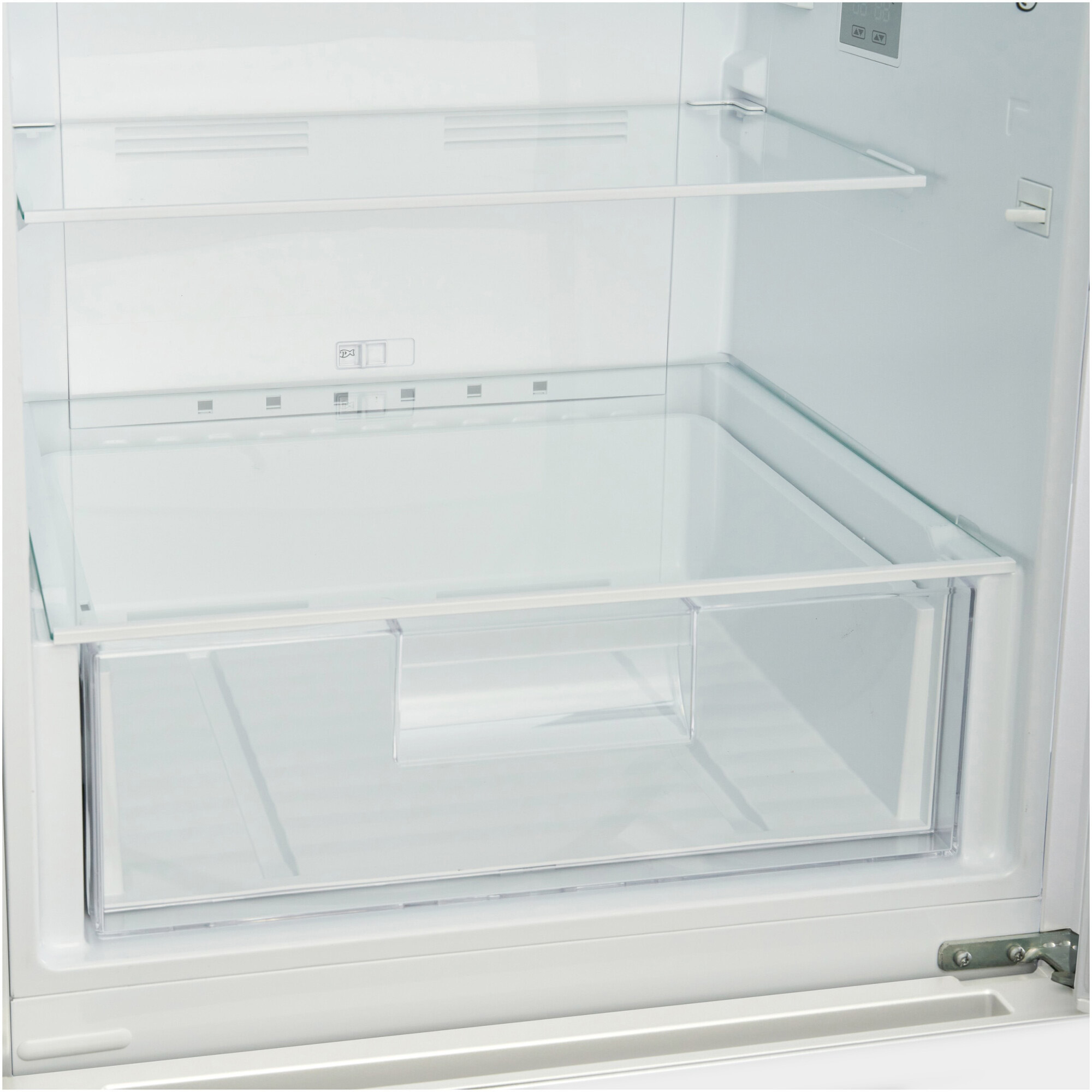 Binnenkant van een witte koelkast. Een groentelade en planken zijn zichtbaar. De binnenkant is schoon en leeg.